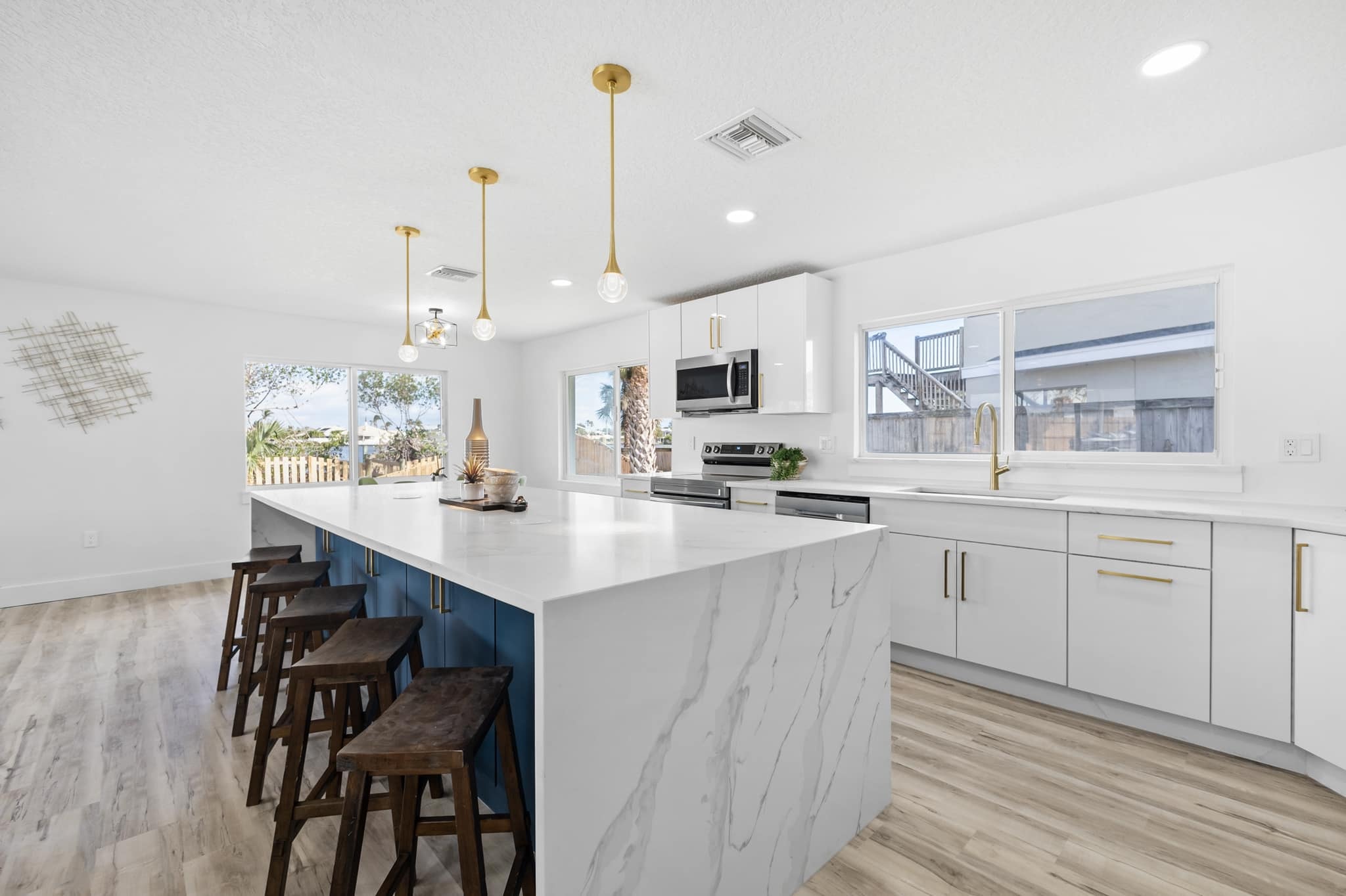 White and navy blue kitchen with marble waterfall island wood bar stools and gold pendants by 1 Stop Cabinets
