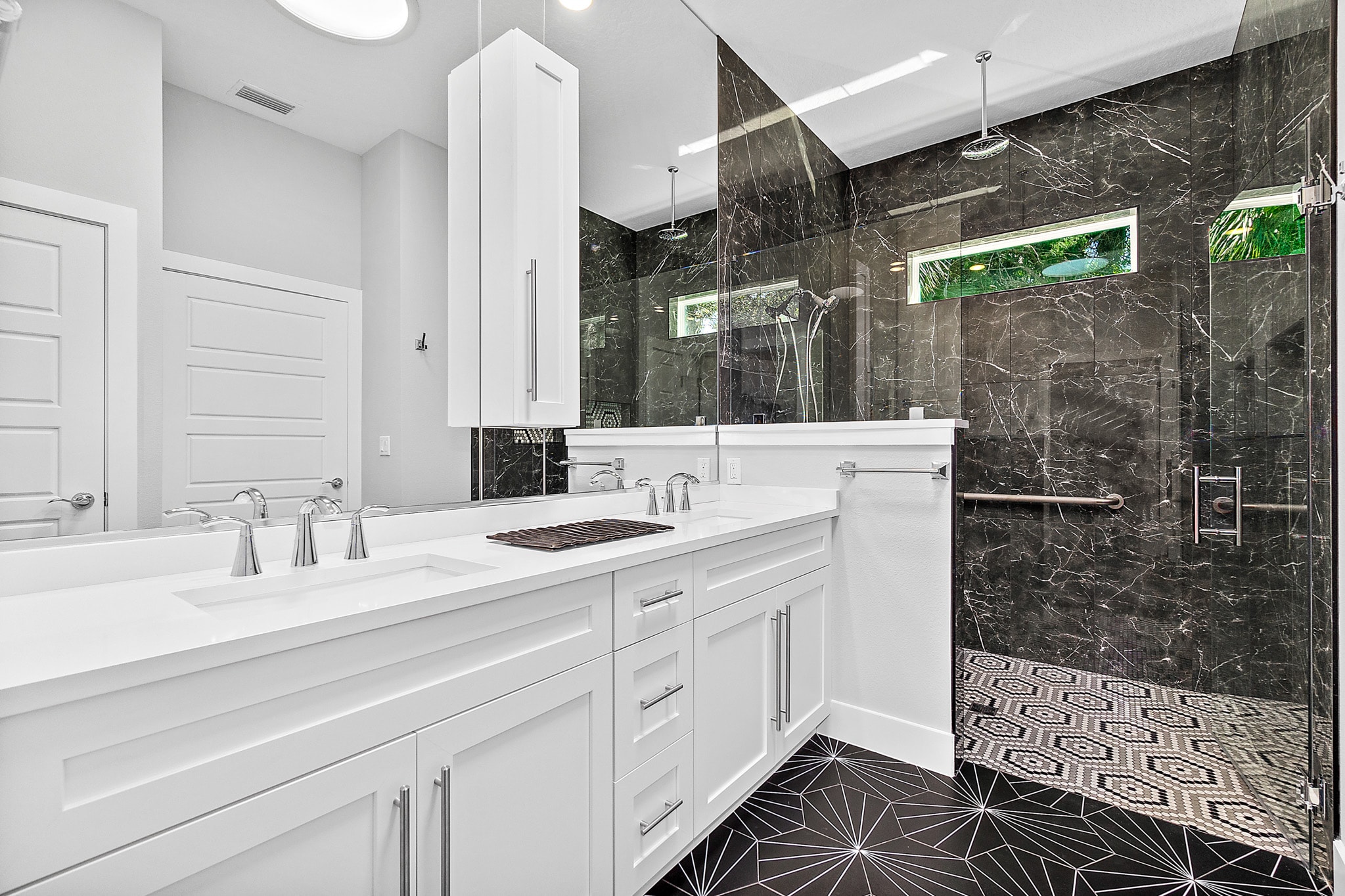 White shaker double vanity with quartz countertop and dramatic black marble shower surround with geometric floor tile by 1 Stop Cabinets