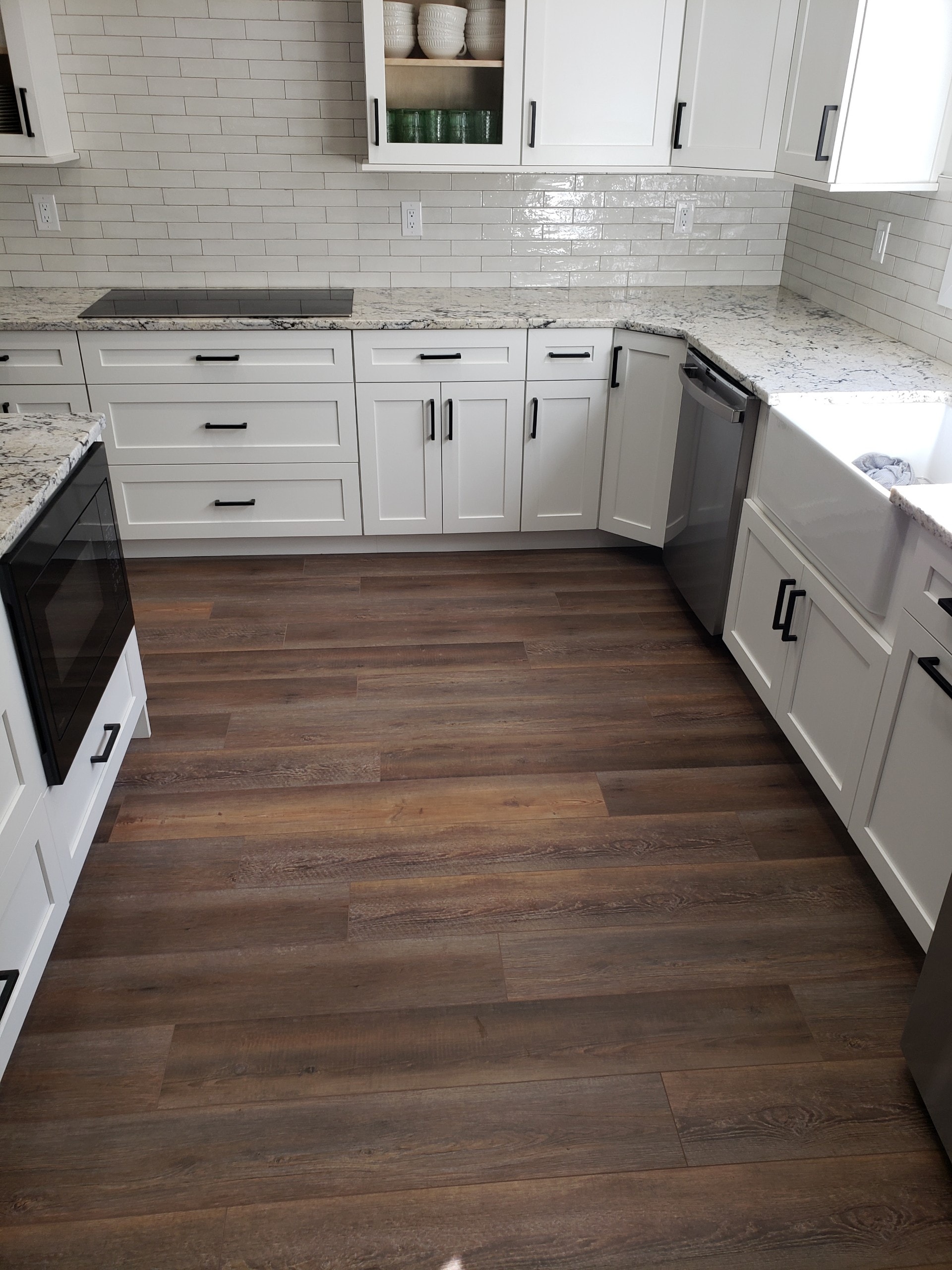 White shaker kitchen with granite countertops black hardware subway tile backsplash and farmhouse sink on hardwood floors by 1 Stop Cabinets