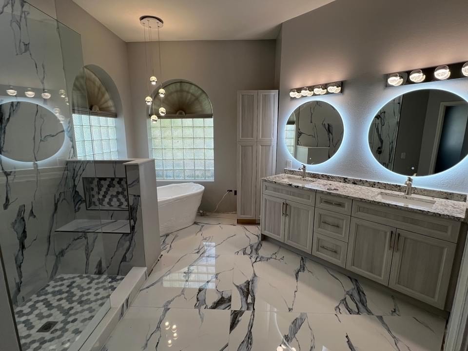 Luxury master bathroom with gray shaker vanity marble floors freestanding tub and LED backlit round mirrors by 1 Stop Cabinets