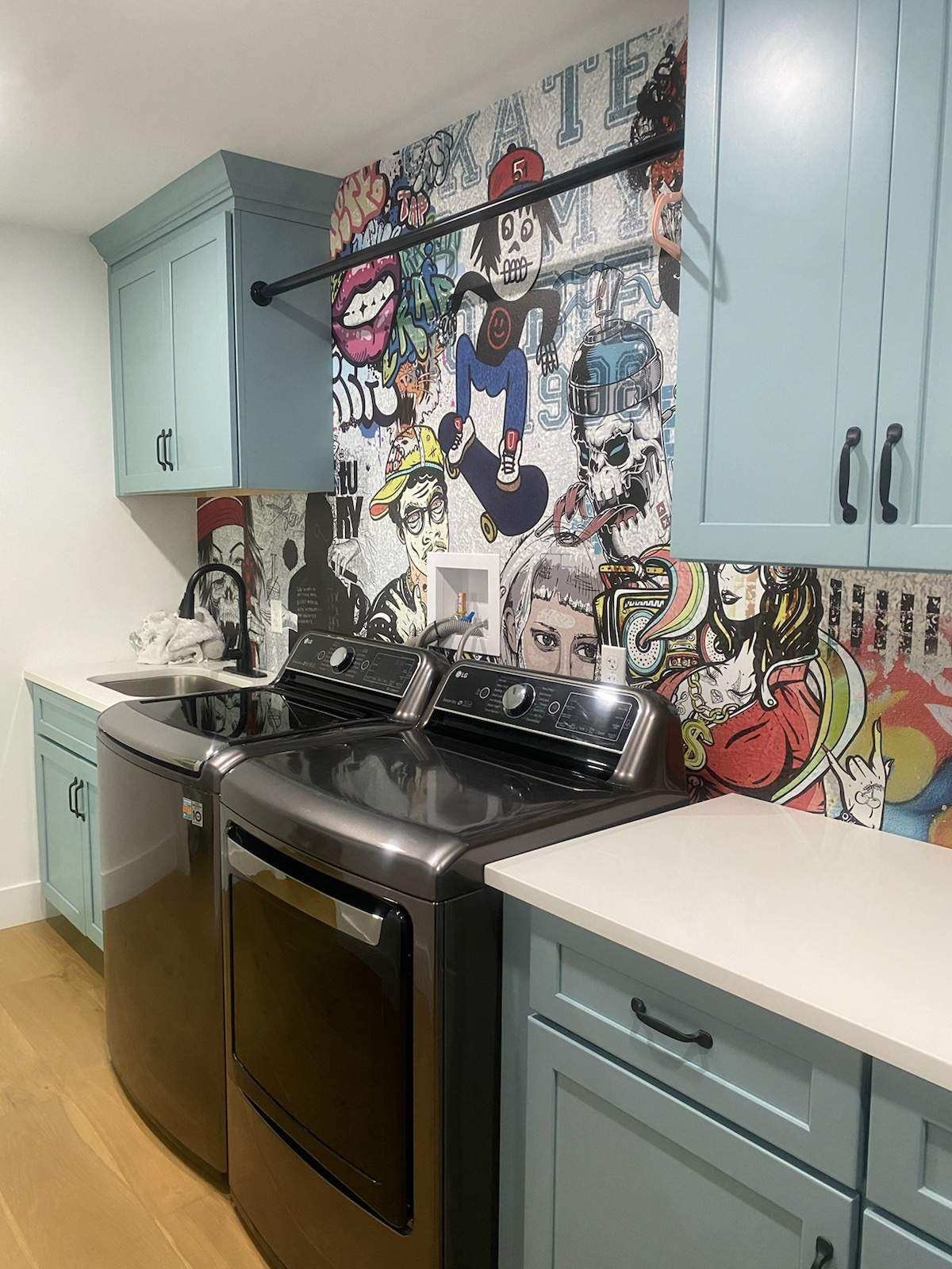 Mint green shaker laundry room with black hardware pop-art graffiti backsplash and LG washer dryer by 1 Stop Cabinets