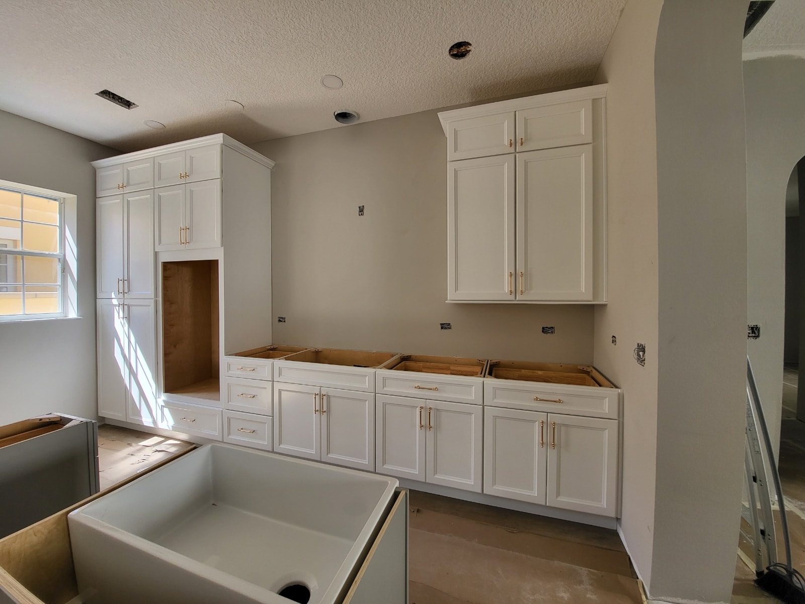 White raised panel kitchen under construction with gold hardware tall pantry and farmhouse sink by 1 Stop Cabinets