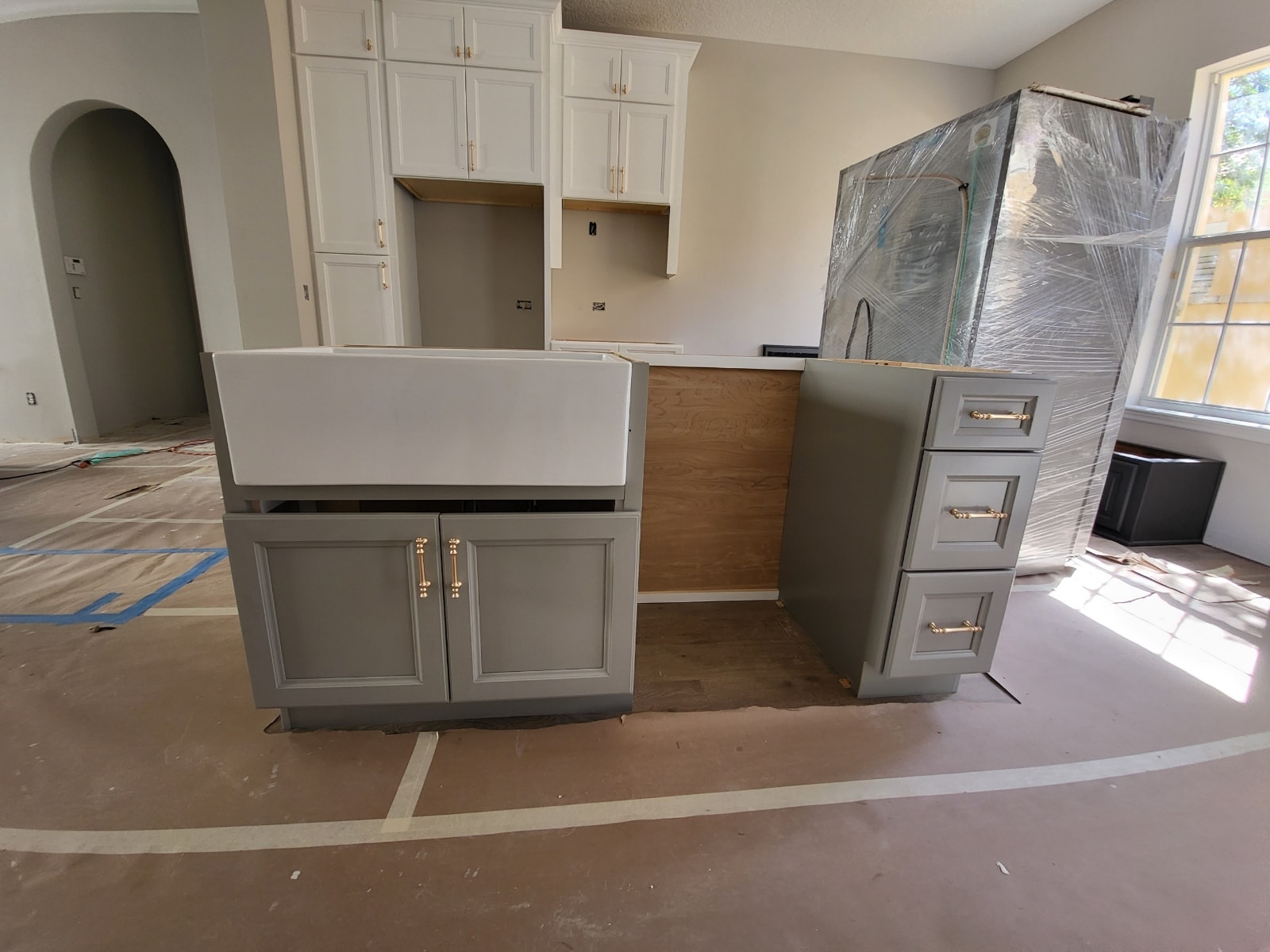 Two-tone white and gray raised panel kitchen under construction with farmhouse sink and gold hardware by 1 Stop Cabinets