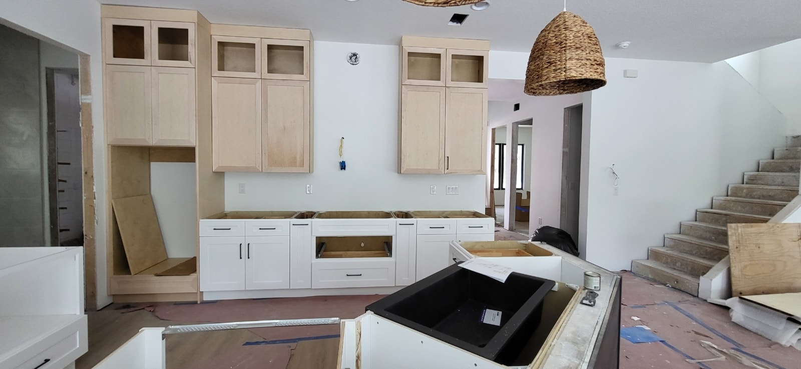 Natural maple and white two-tone new construction kitchen under construction with black farmhouse sink and woven pendant by 1 Stop Cabinets