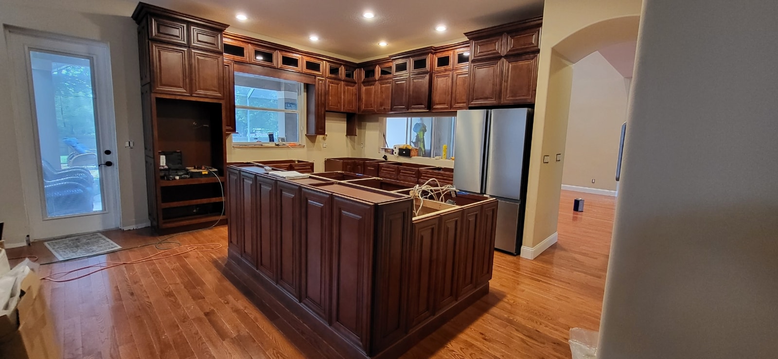 Rich cherry raised panel kitchen under construction with large island crown molding and hardwood floors by 1 Stop Cabinets