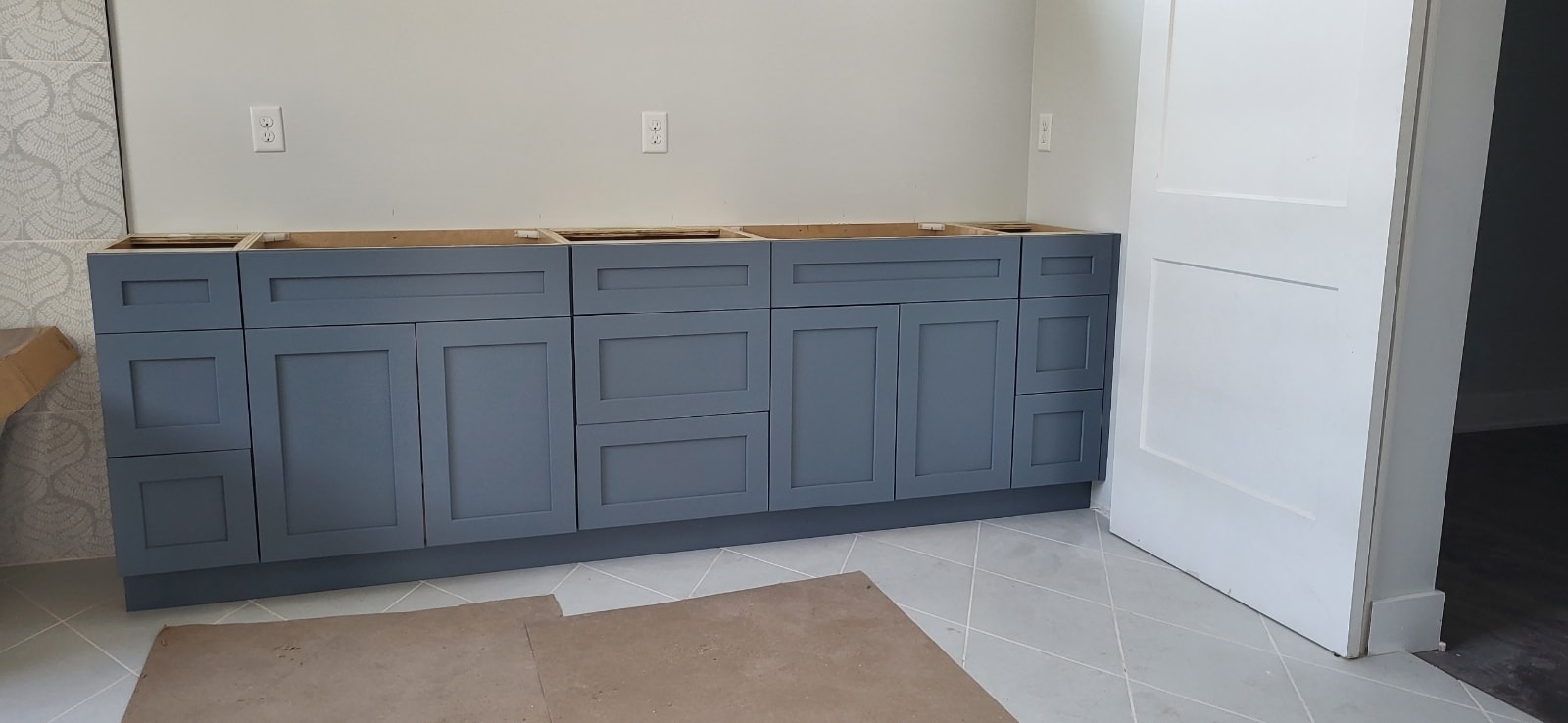 Slate blue shaker bathroom vanity base cabinets under construction on white tile floor by 1 Stop Cabinets