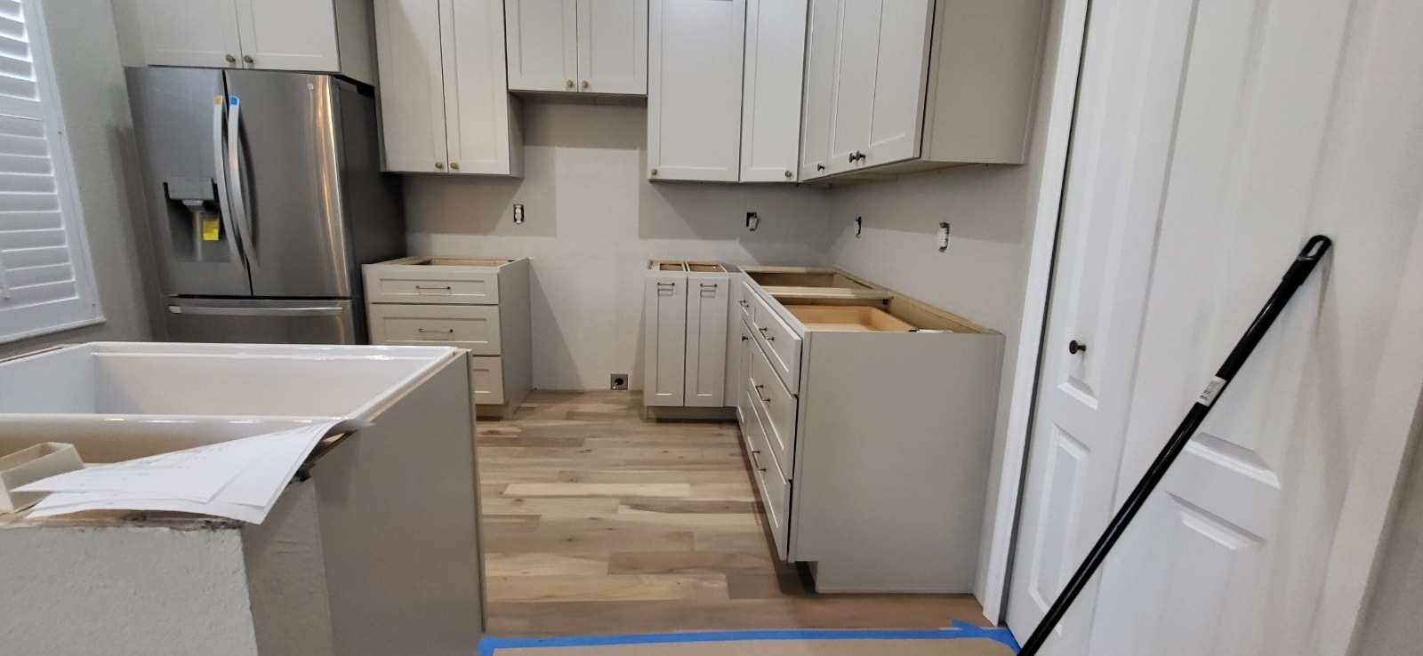 White shaker kitchen under construction with stainless refrigerator and light wood floors by 1 Stop Cabinets