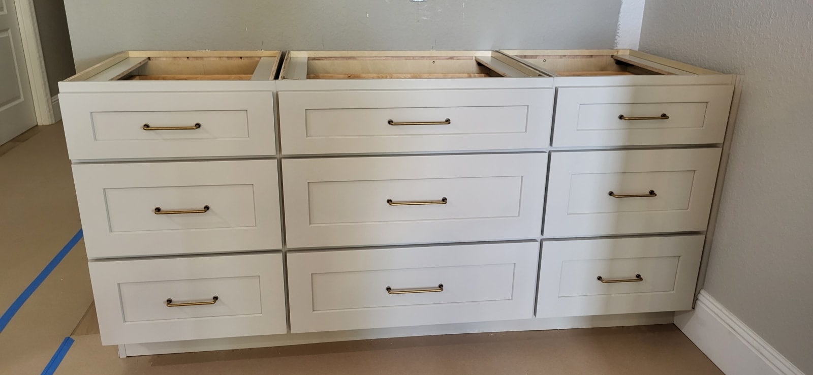 White shaker bathroom vanity base cabinets under construction with nine drawers and brass hardware by 1 Stop Cabinets