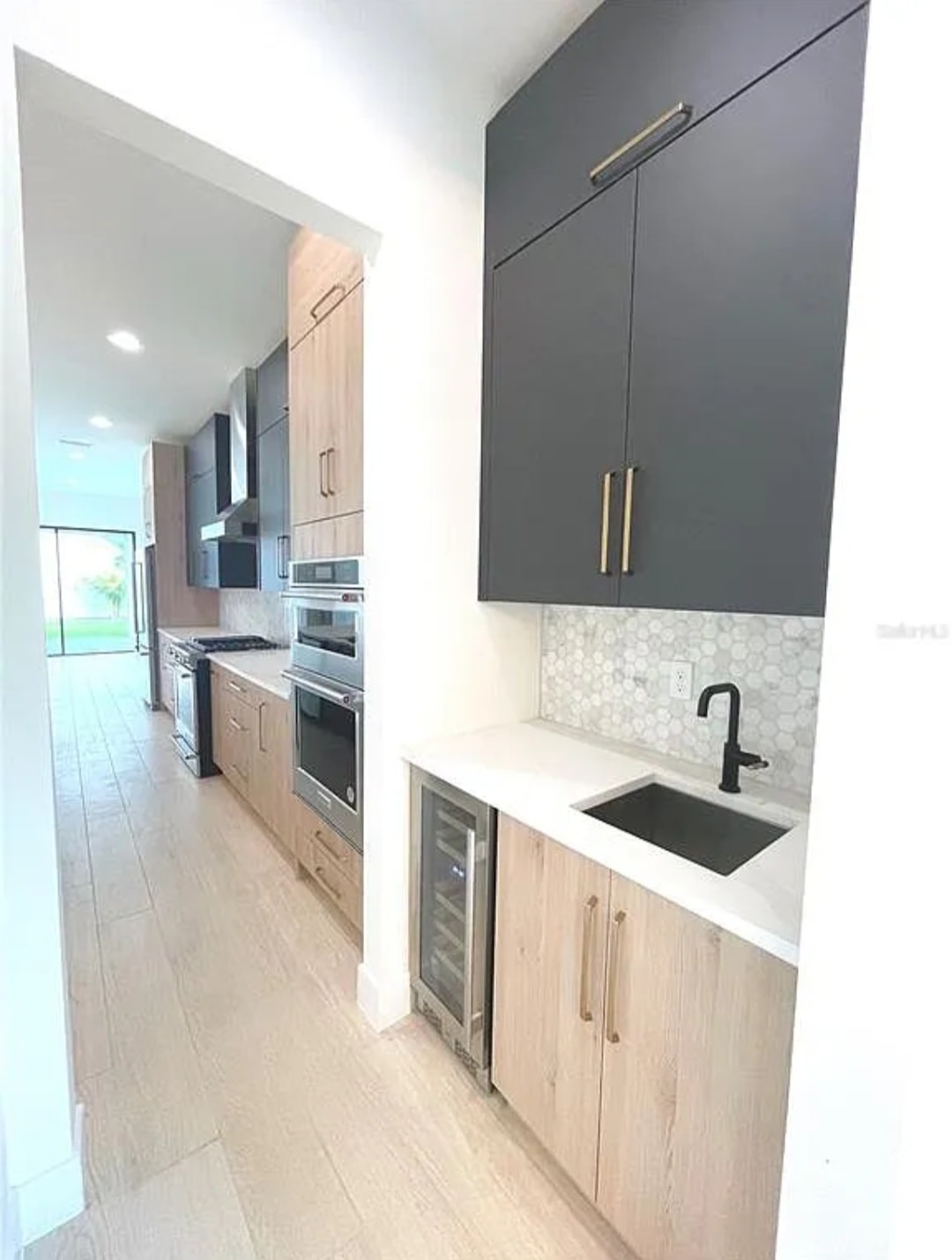 Two-tone charcoal and natural oak kitchen butler pantry with wine cooler black sink and hexagon tile backsplash by 1 Stop Cabinets