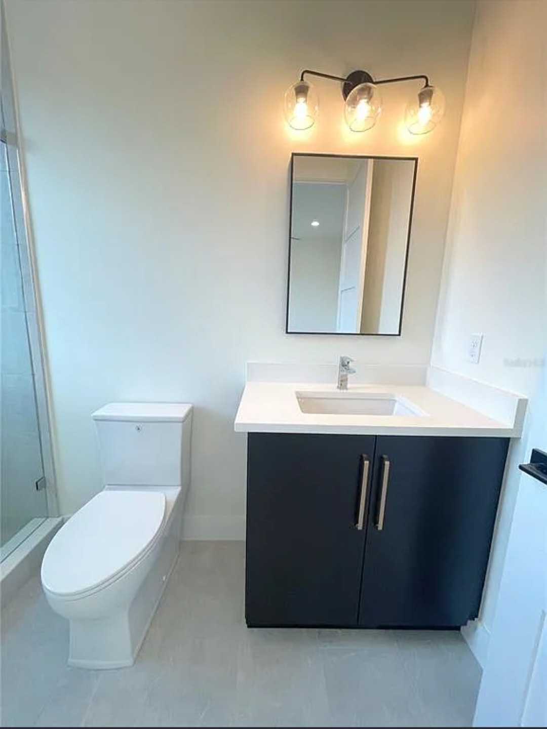 Dark flat panel bathroom vanity with white quartz countertop black framed mirror and glass shower by 1 Stop Cabinets