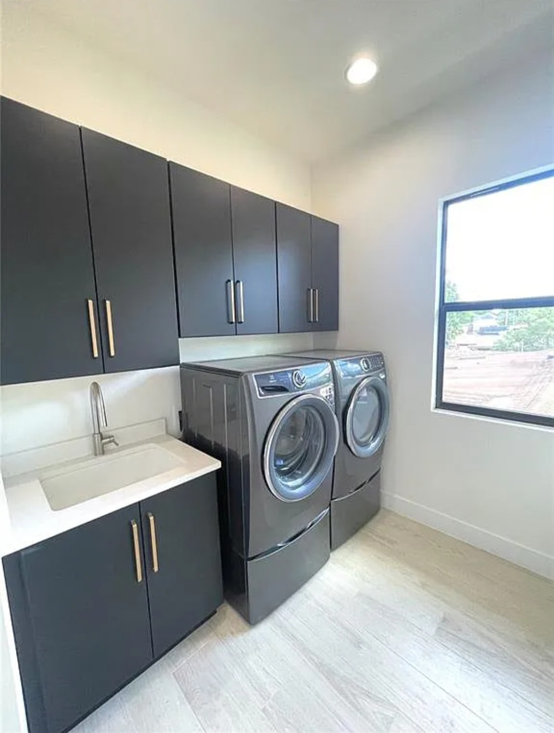 Dark flat panel laundry room with quartz countertop utility sink gold hardware and Electrolux washer dryer by 1 Stop Cabinets