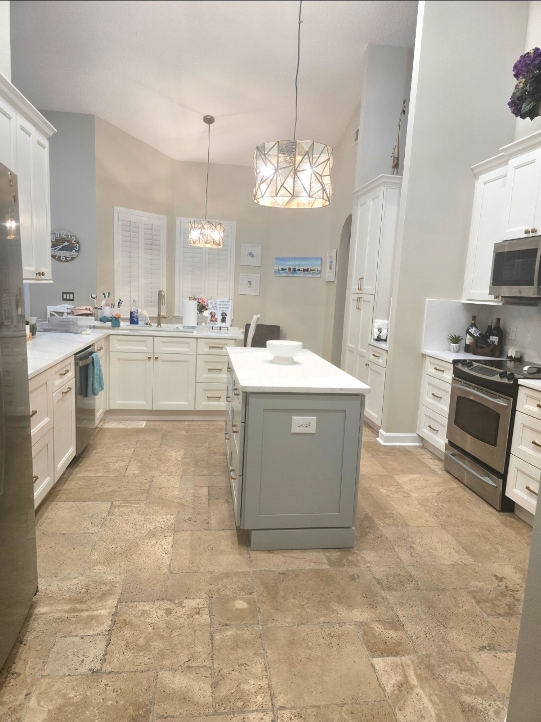 White raised panel kitchen with gray island quartz countertops geometric pendant lights and travertine tile floors by 1 Stop Cabinets