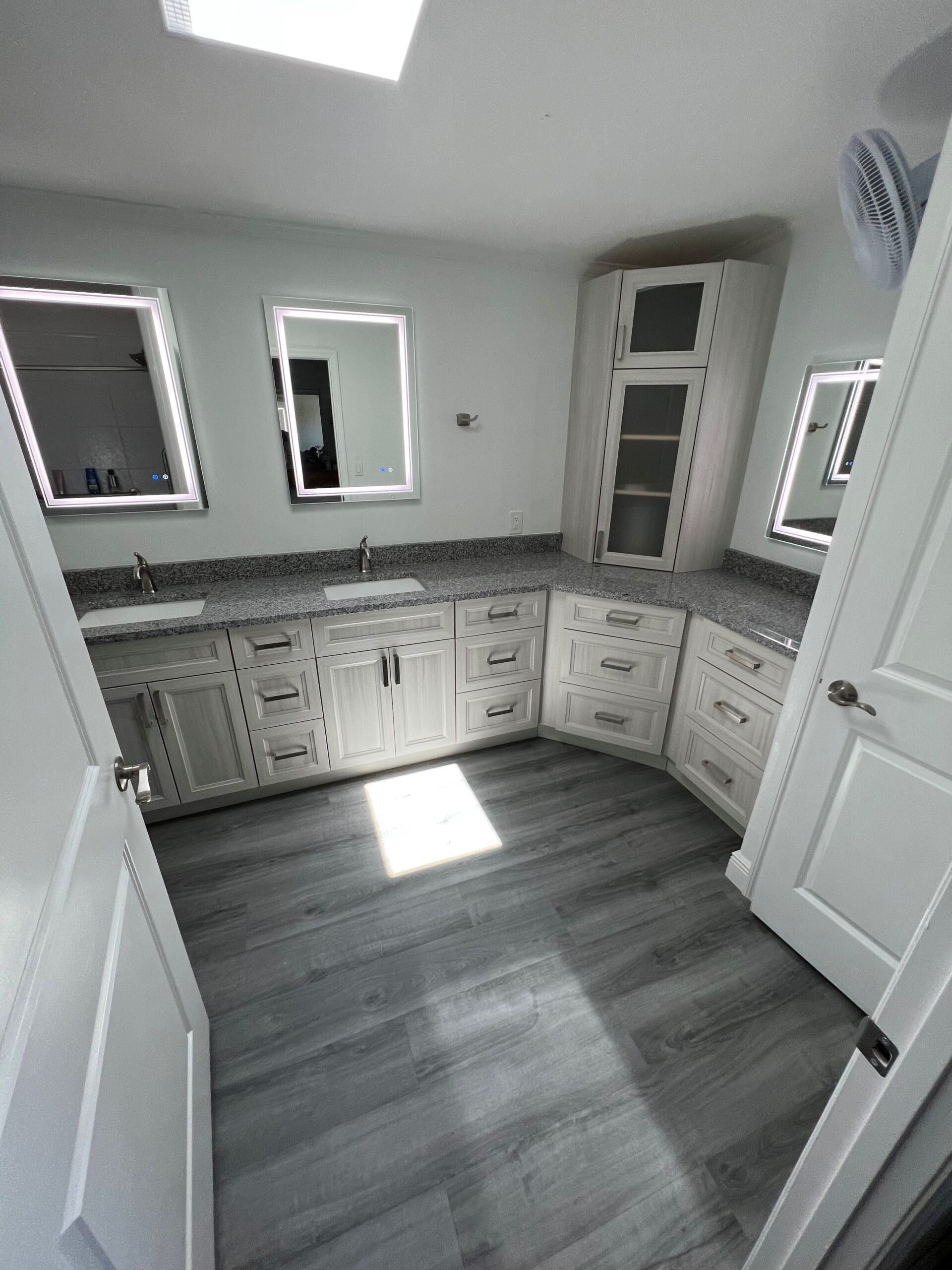 Large L-shaped gray raised panel bathroom with granite countertops corner tower cabinet LED mirrors and skylight by 1 Stop Cabinets