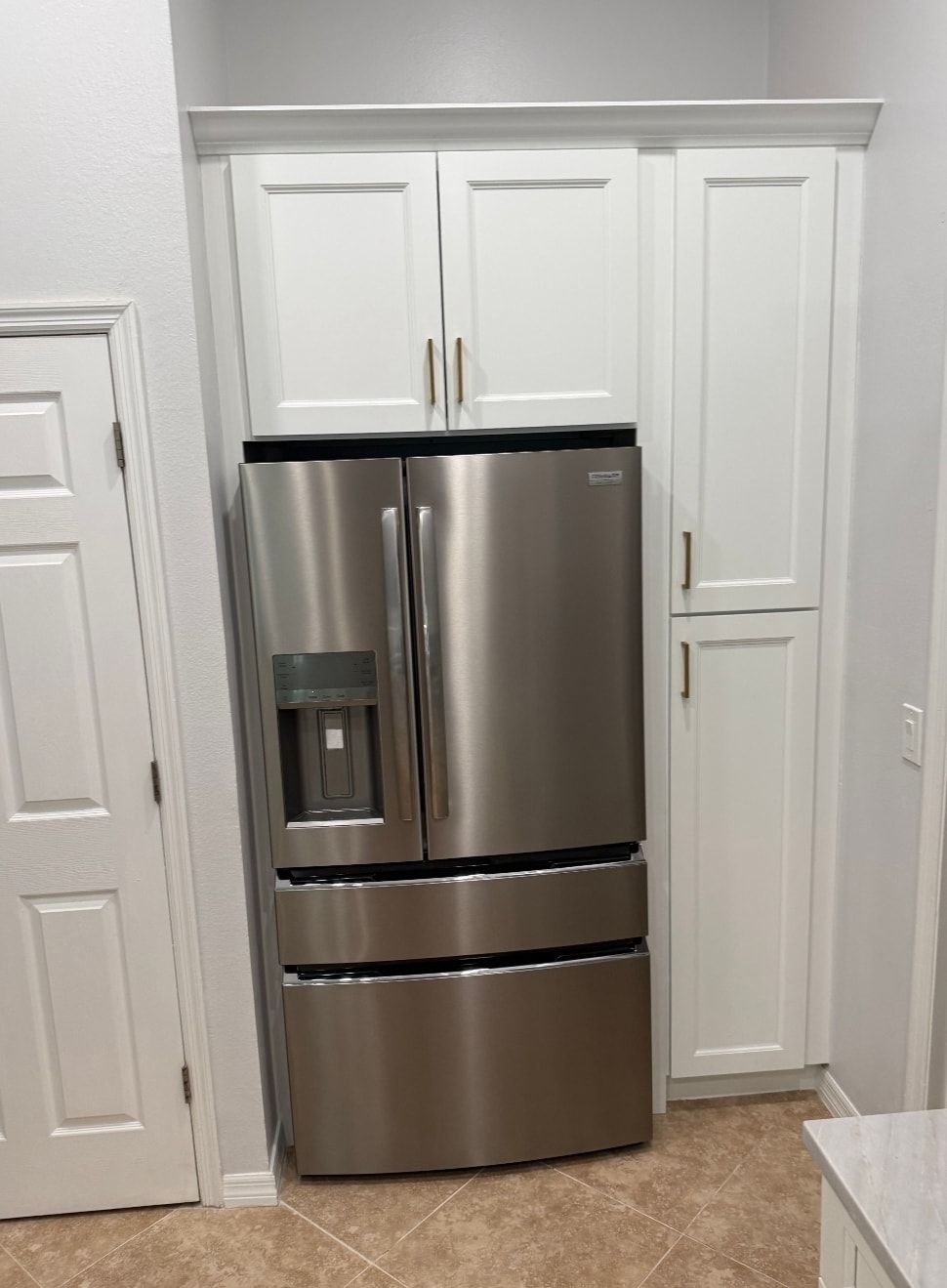 White raised panel kitchen refrigerator wall with built-in upper cabinets tall pantry surround and gold hardware by 1 Stop Cabinets