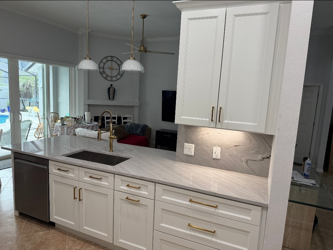 White raised panel open-concept kitchen with marble quartz peninsula black undermount sink gold faucet and pendant lights by 1 Stop Cabinets