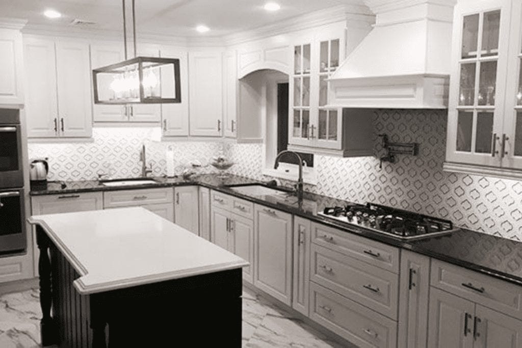 White kitchen with black countertops and patterned backsplash by 1 Stop Cabinets