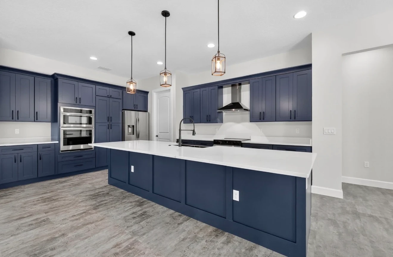 Bold navy blue shaker kitchen with white quartz island black hardware double wall ovens stainless refrigerator and copper lantern pendants by 1 Stop Cabinets