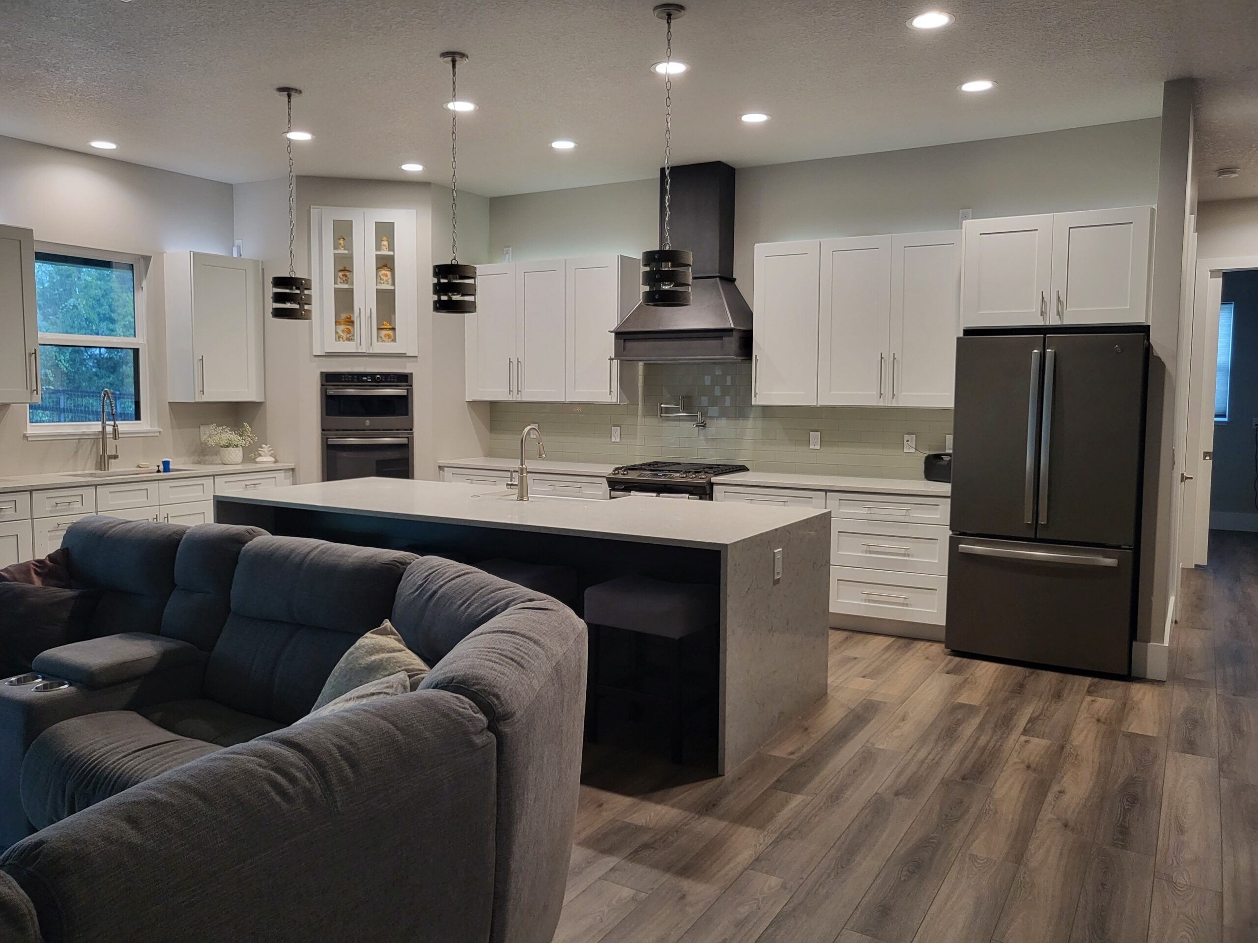 White shaker kitchen with dark island and open concept living by 1 Stop Cabinets