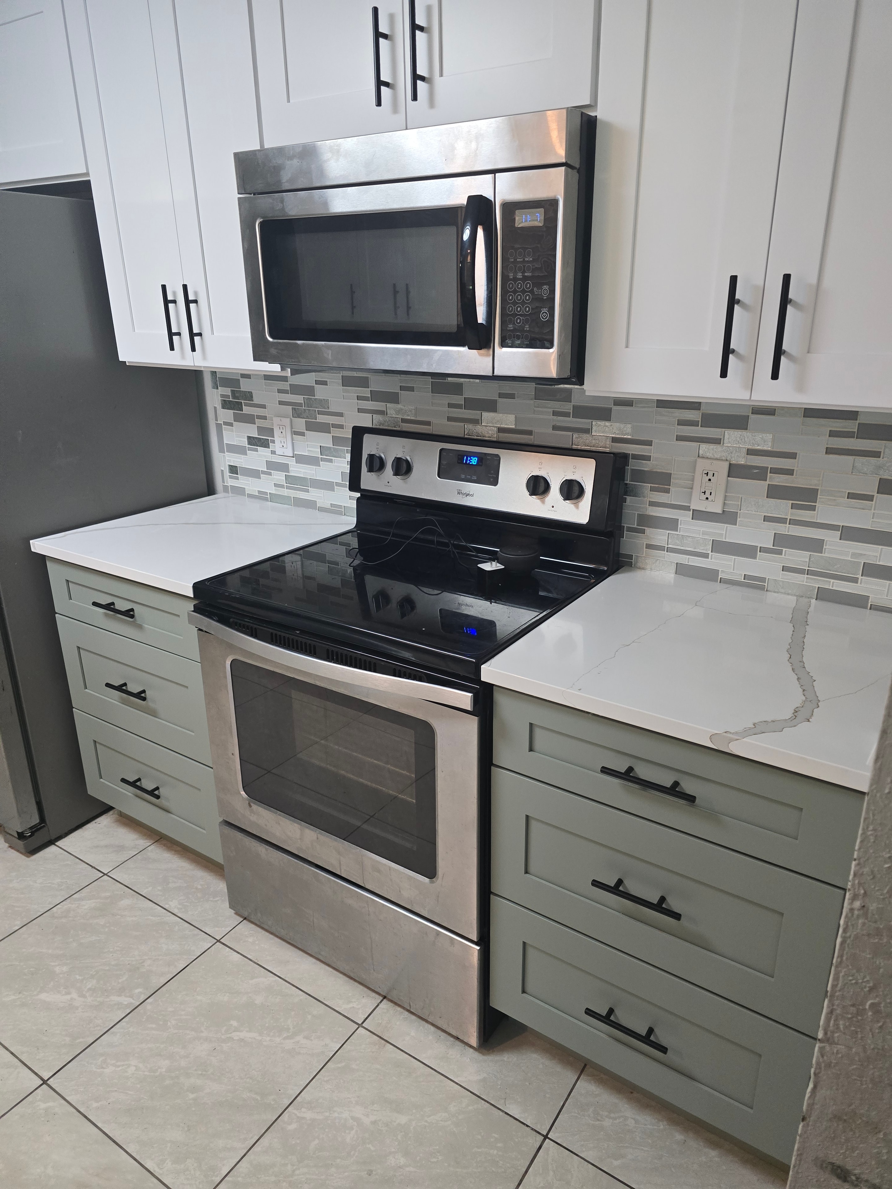 Two-tone kitchen with white and sage green shaker cabinets and mosaic backsplash by 1 Stop Cabinets