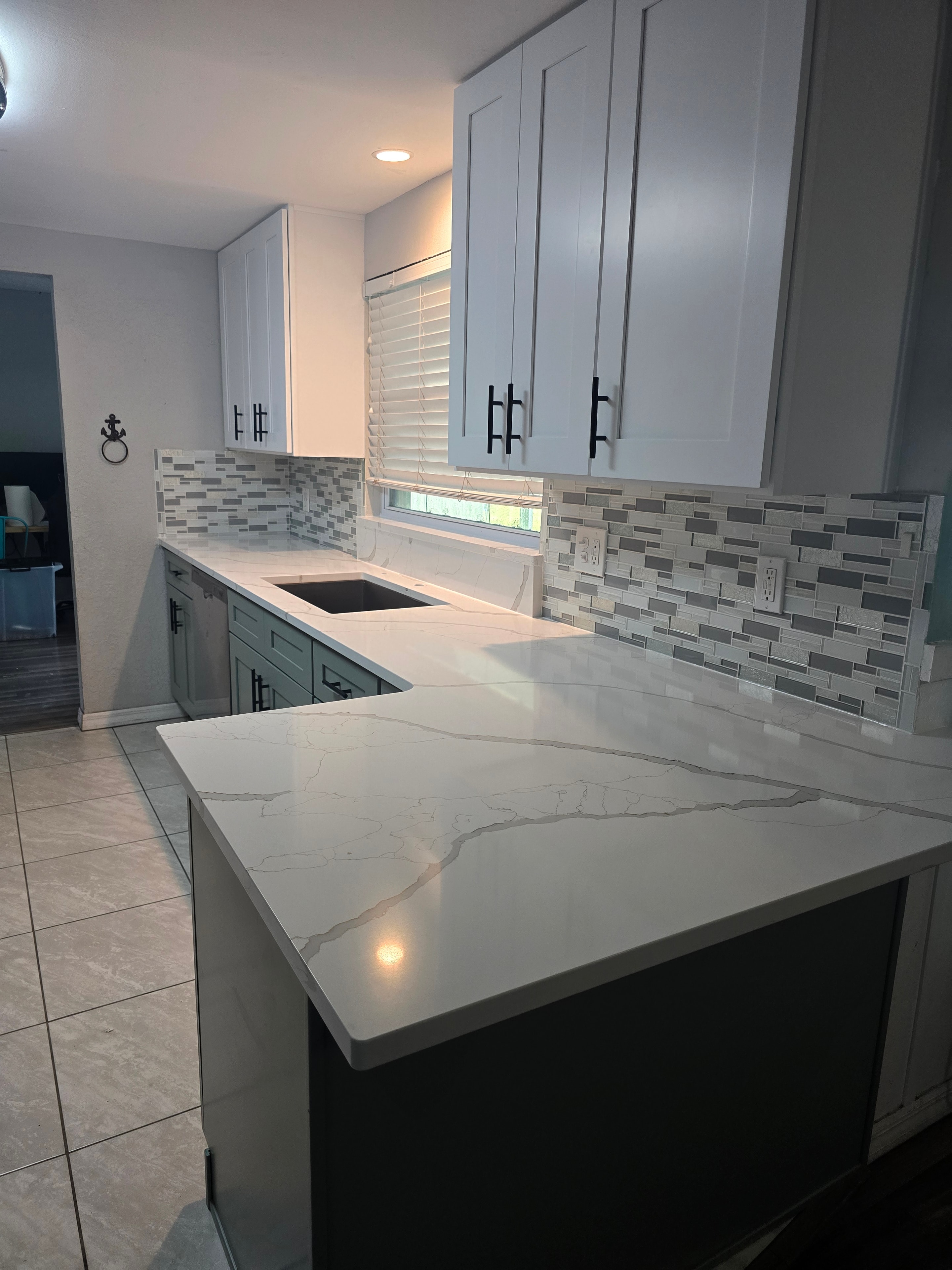 White shaker kitchen with quartz waterfall island and mosaic backsplash by 1 Stop Cabinets