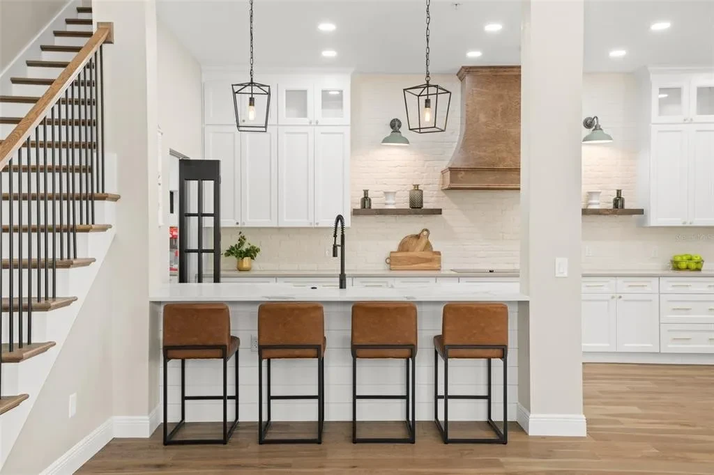 White shaker kitchen with wood range hood and leather bar stools by 1 Stop Cabinets