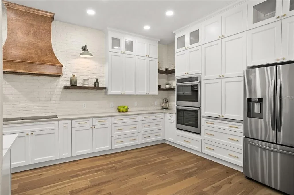 White shaker kitchen with copper range hood detail and brick backsplash by 1 Stop Cabinets