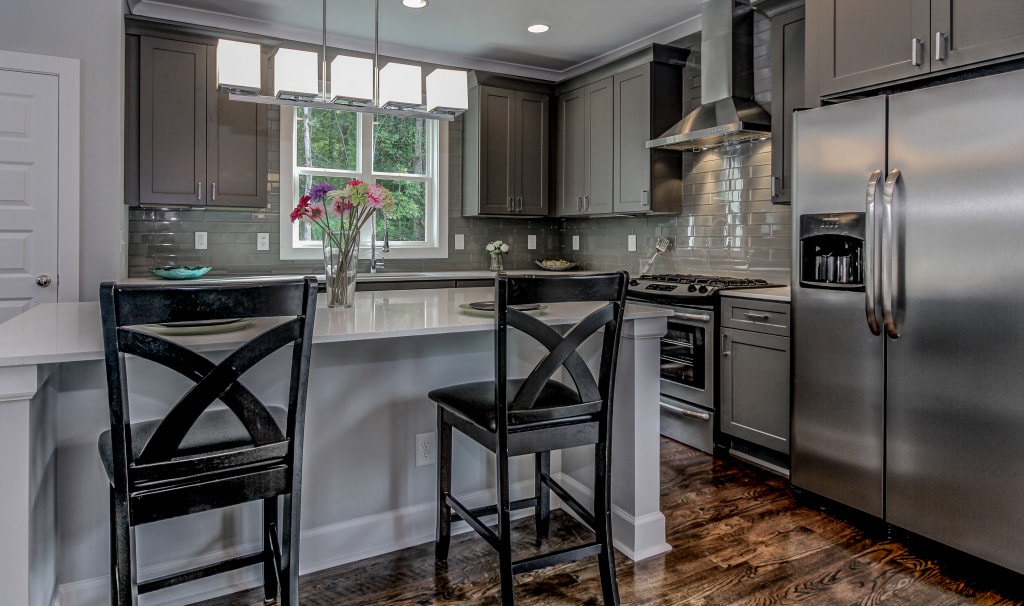 Gray shaker kitchen with white quartz island and black bar stools by 1 Stop Cabinets