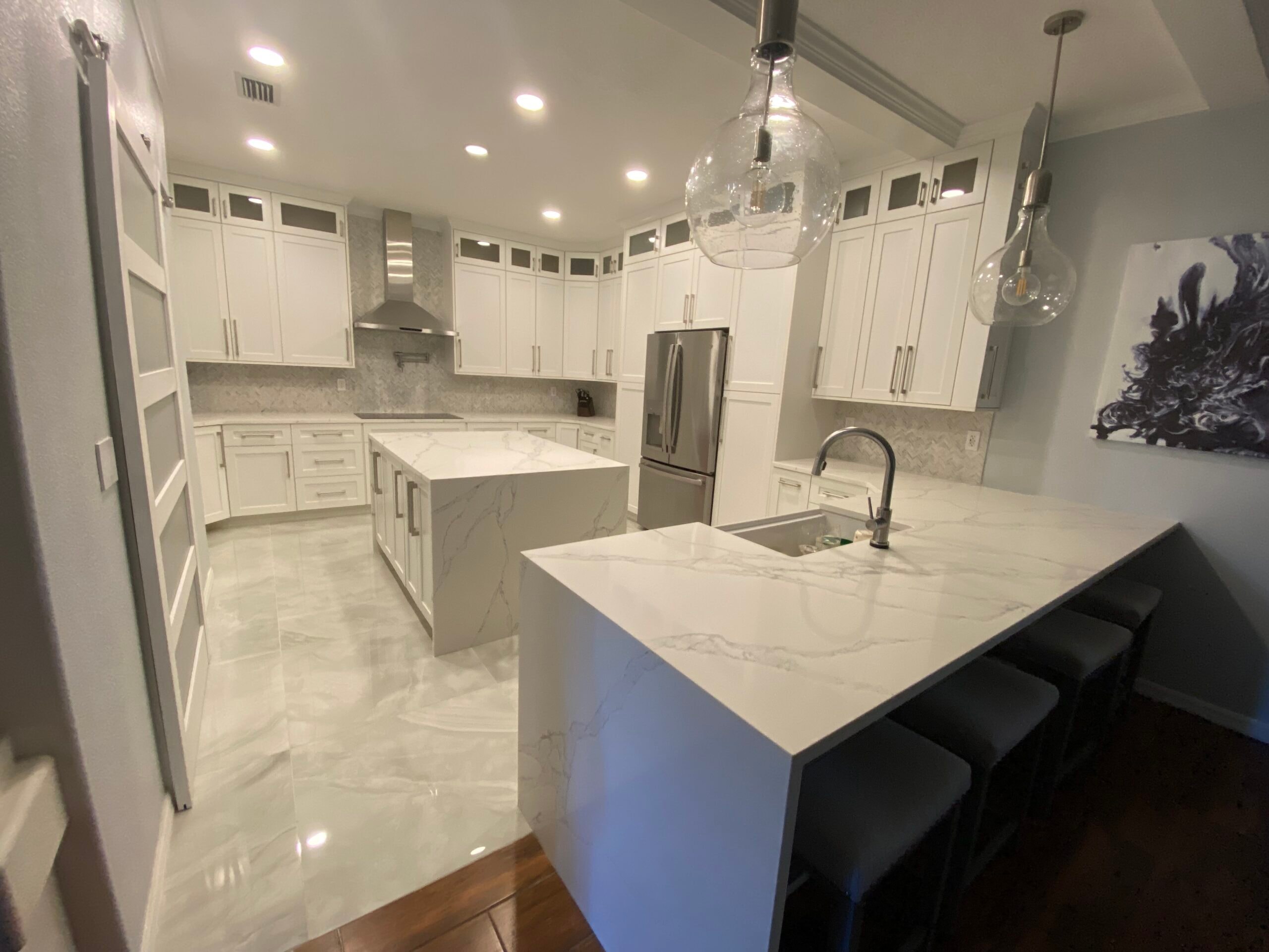 White shaker kitchen with marble waterfall island and glass pendant lights by 1 Stop Cabinets