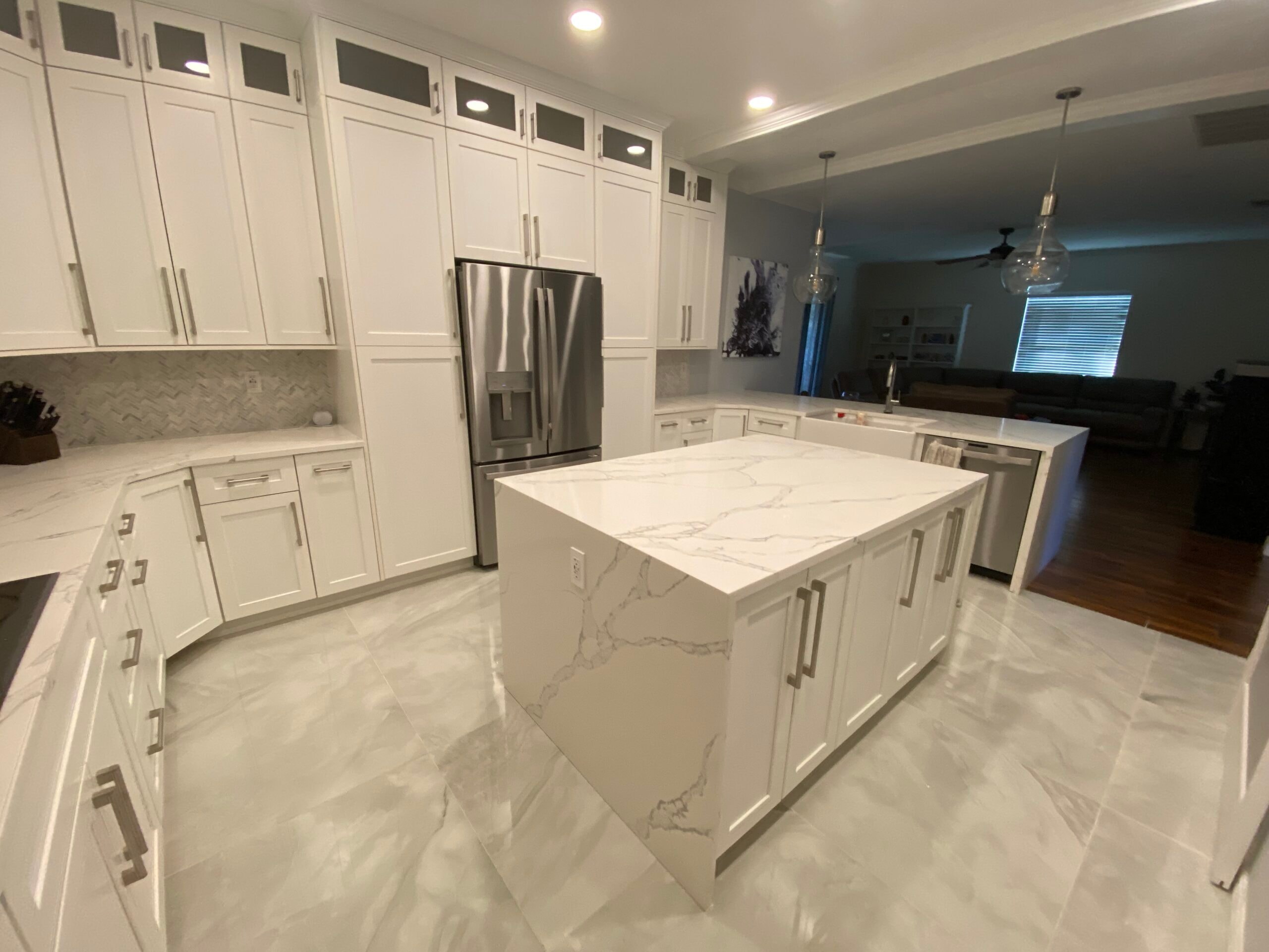 White shaker kitchen with marble island and herringbone backsplash by 1 Stop Cabinets