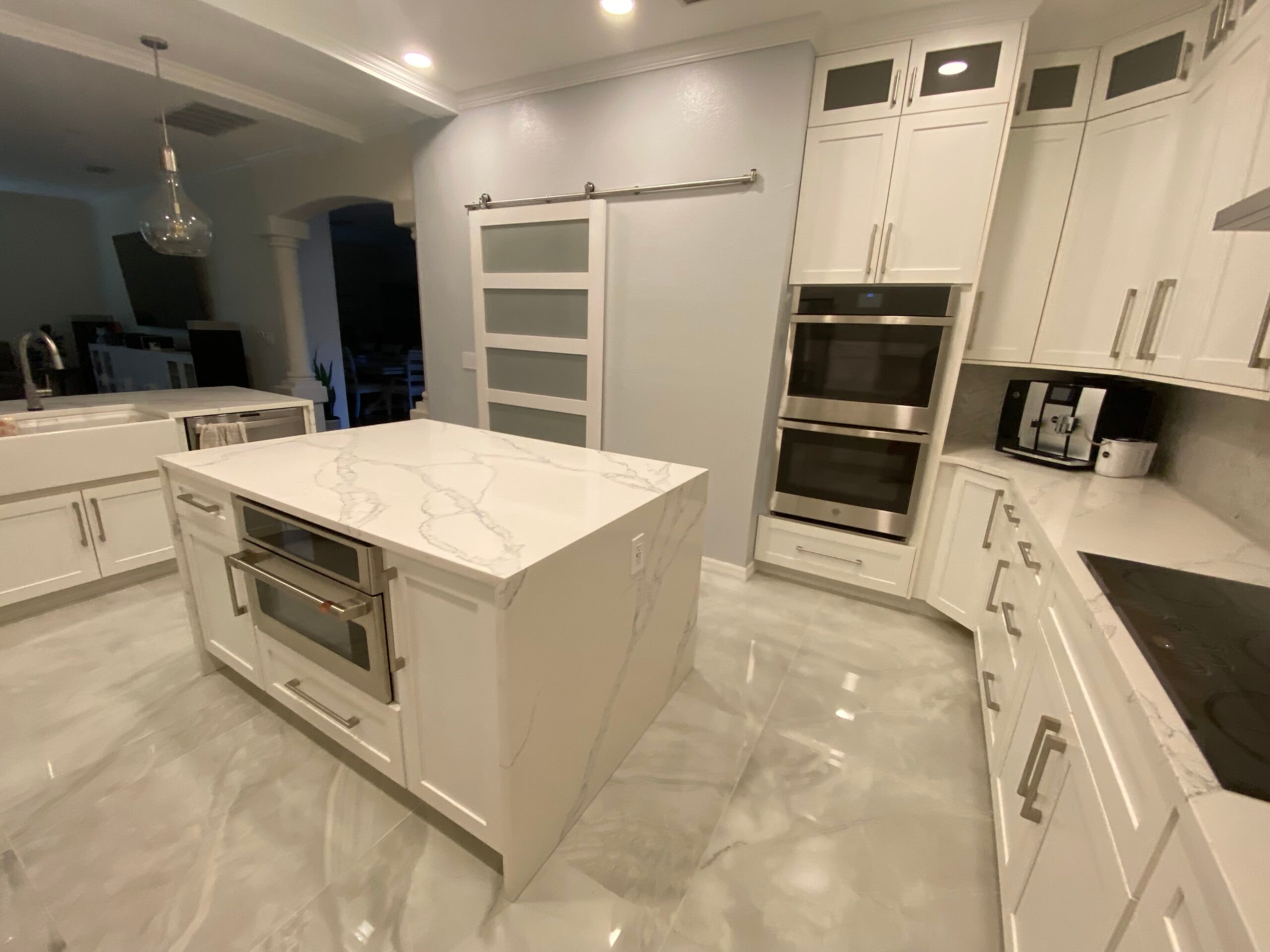White shaker kitchen with marble island and double wall ovens by 1 Stop Cabinets