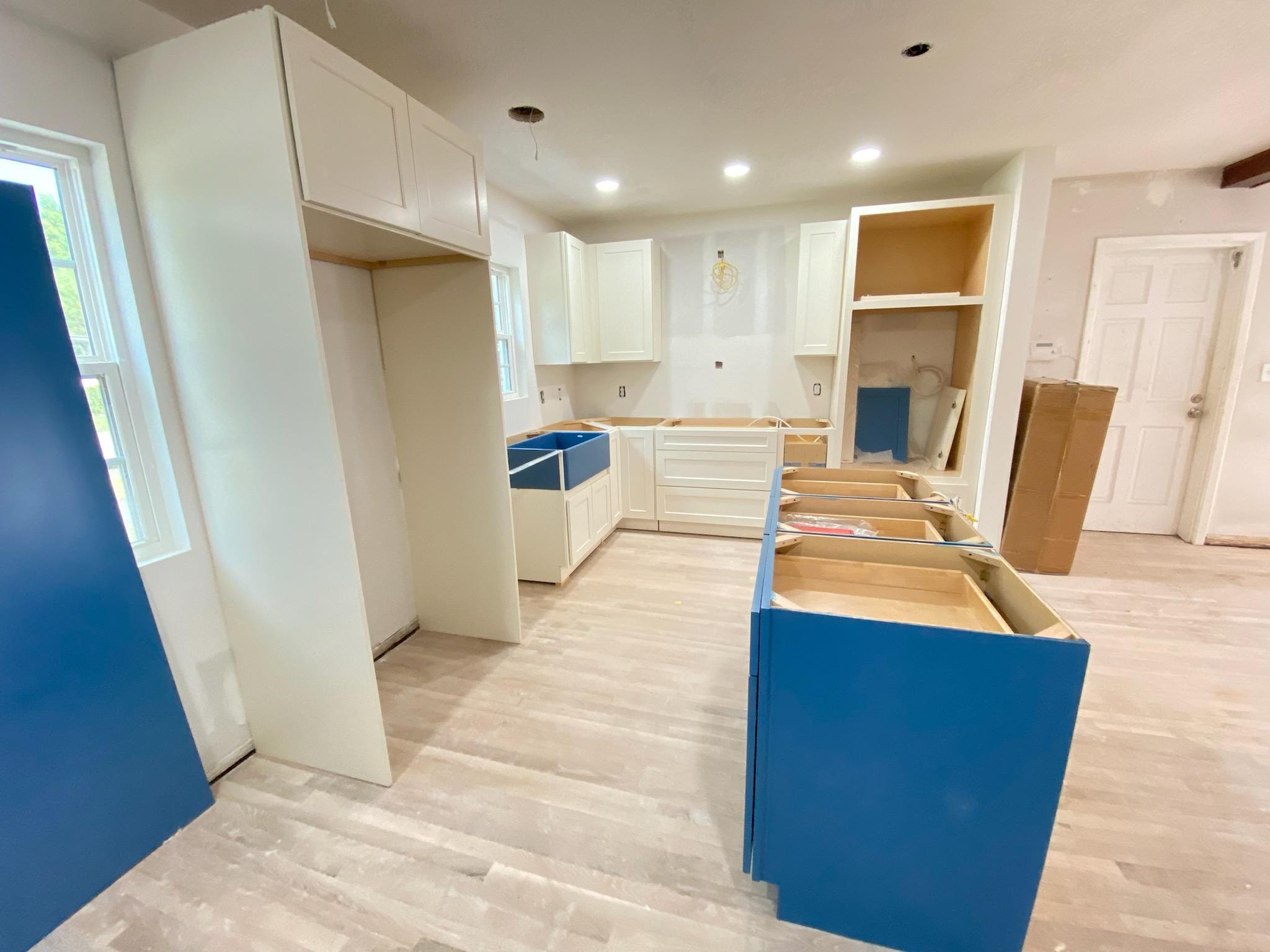 White shaker kitchen under construction with blue island and farmhouse sink by 1 Stop Cabinets