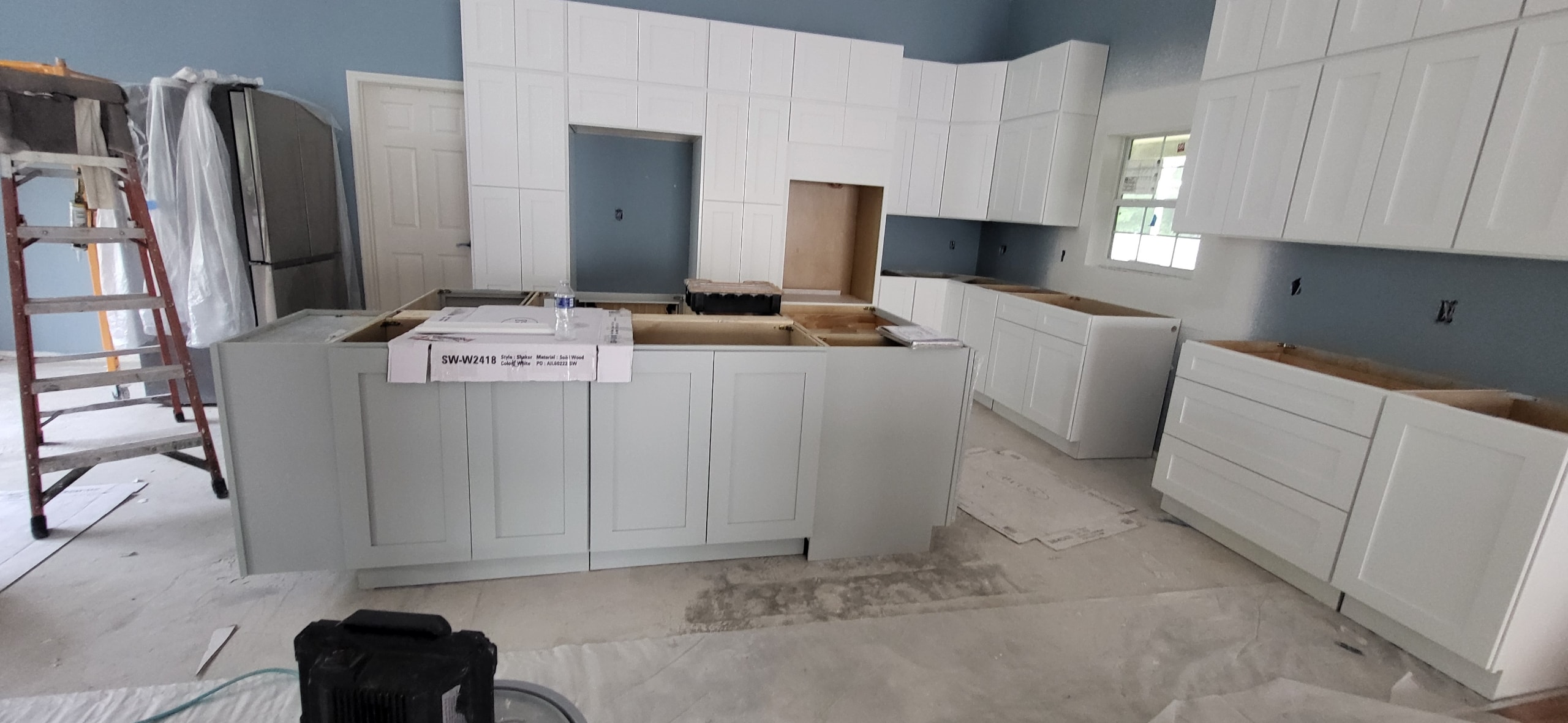 White shaker kitchen under construction with large island by 1 Stop Cabinets