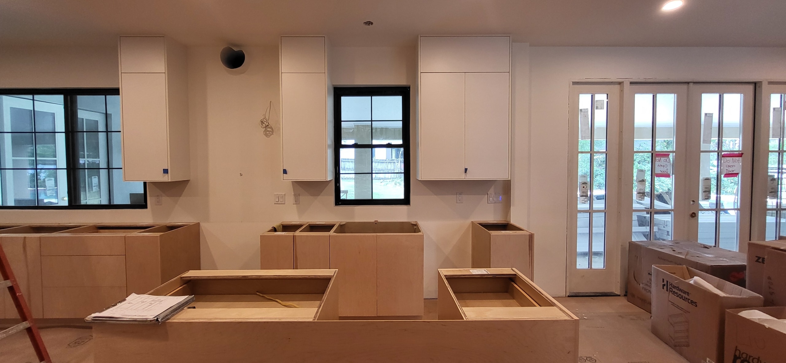 White flat panel kitchen under construction with black window frames and French doors by 1 Stop Cabinets