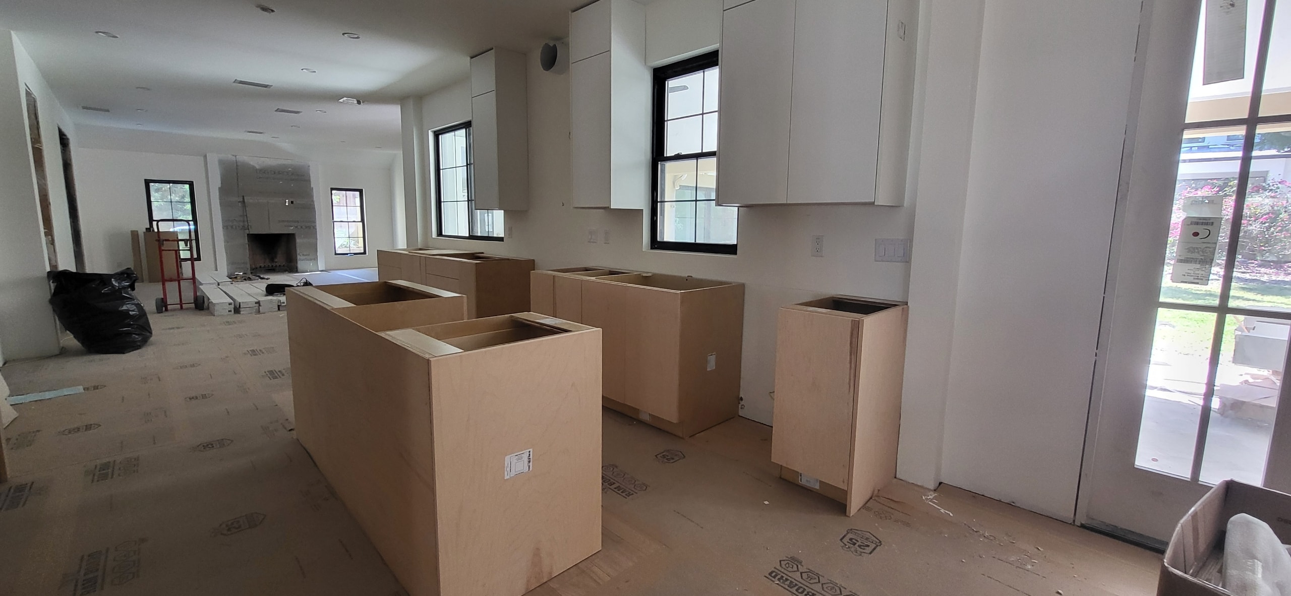White flat panel kitchen under construction with large island and black window frames by 1 Stop Cabinets