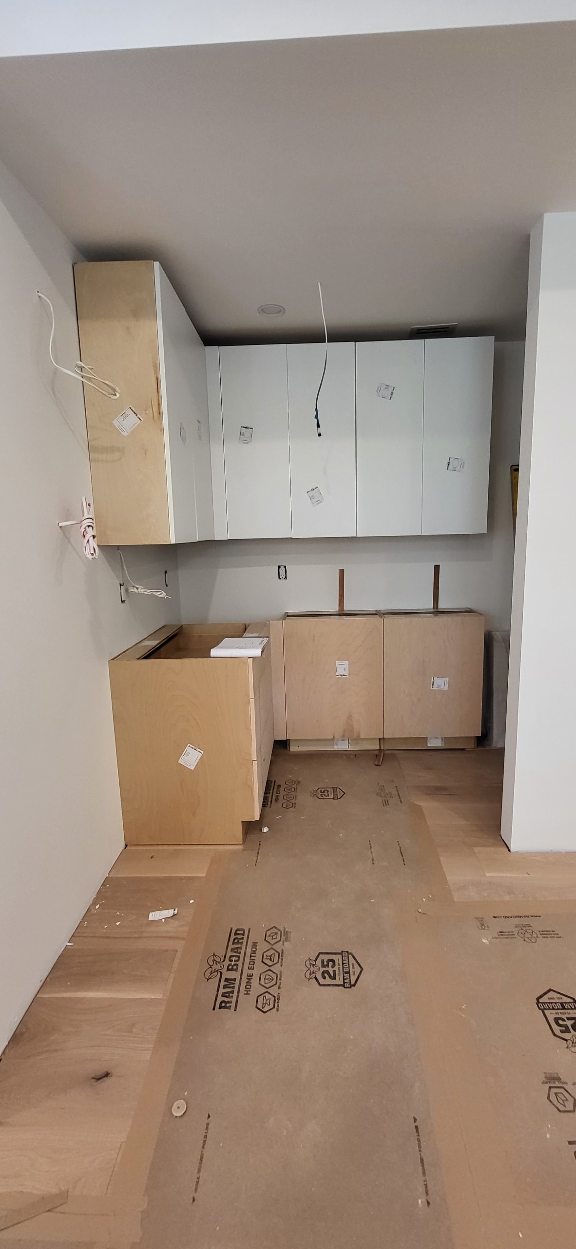 White flat panel upper cabinets being installed in kitchen under construction by 1 Stop Cabinets