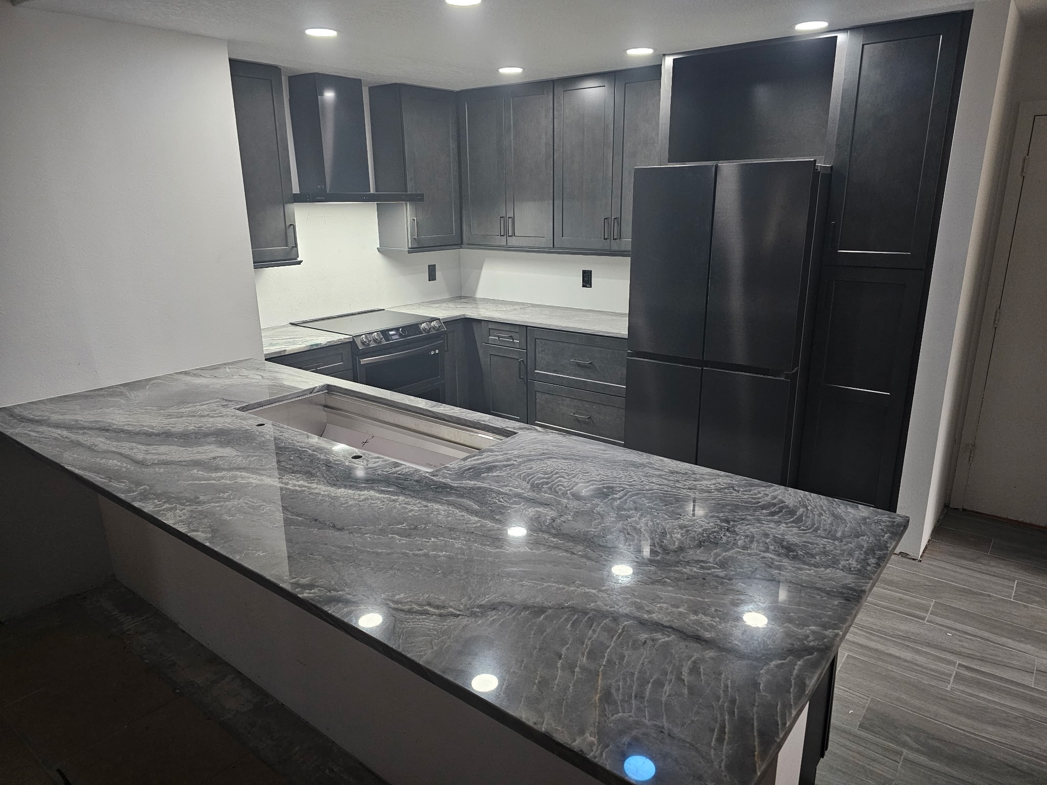 Dark gray shaker kitchen with dramatic quartzite island and under-counter lighting by 1 Stop Cabinets