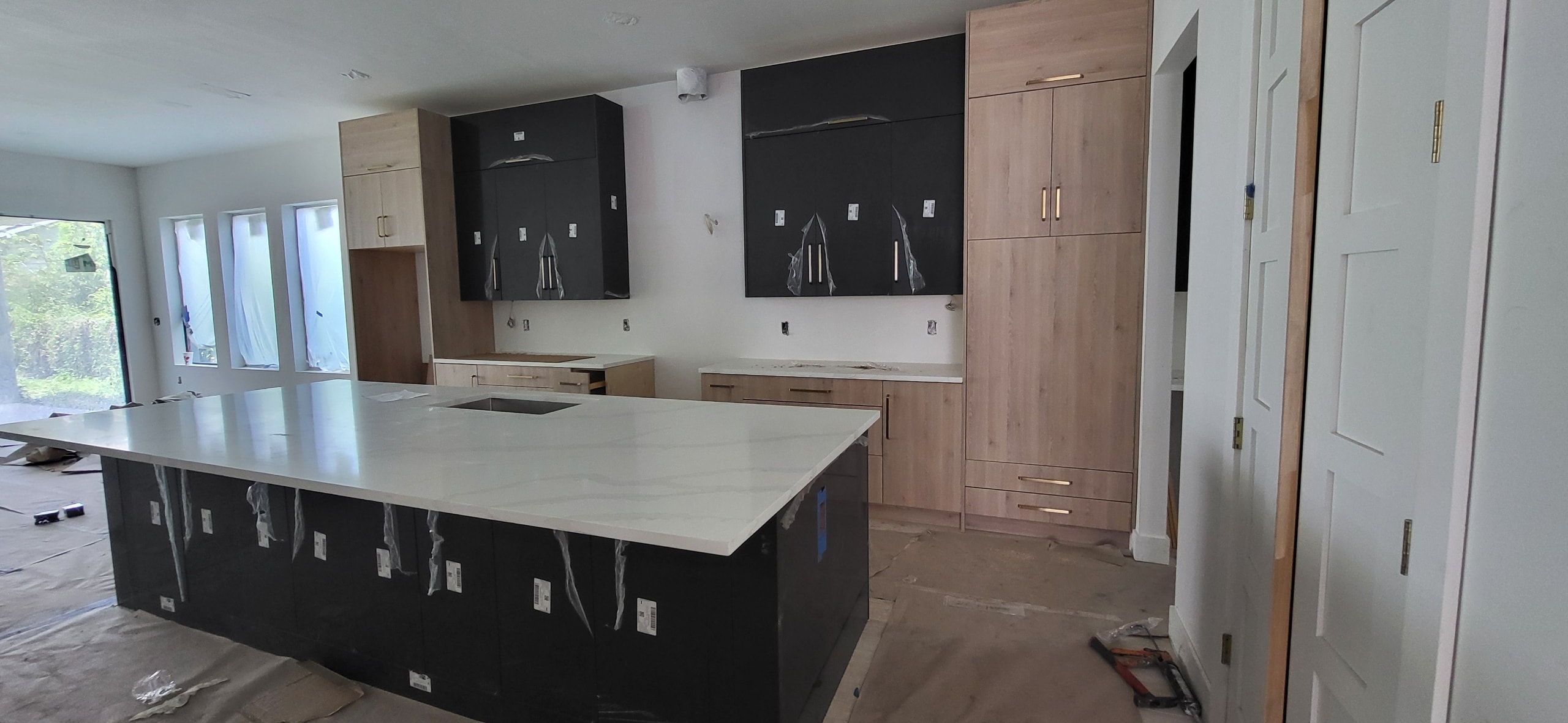 Two-tone black and natural oak kitchen under construction with white quartz island by 1 Stop Cabinets