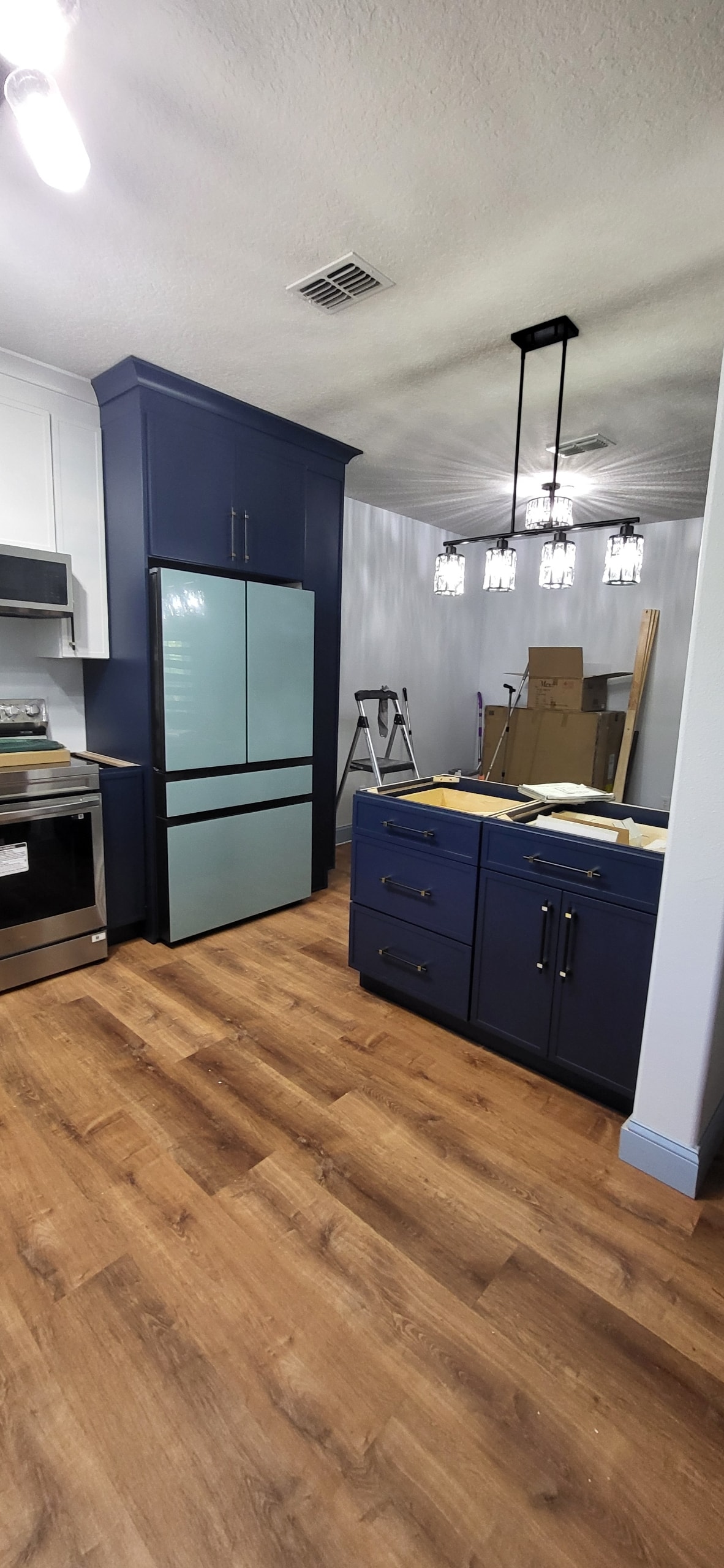 Navy blue shaker kitchen under construction with mint green refrigerator and crystal chandeliers by 1 Stop Cabinets