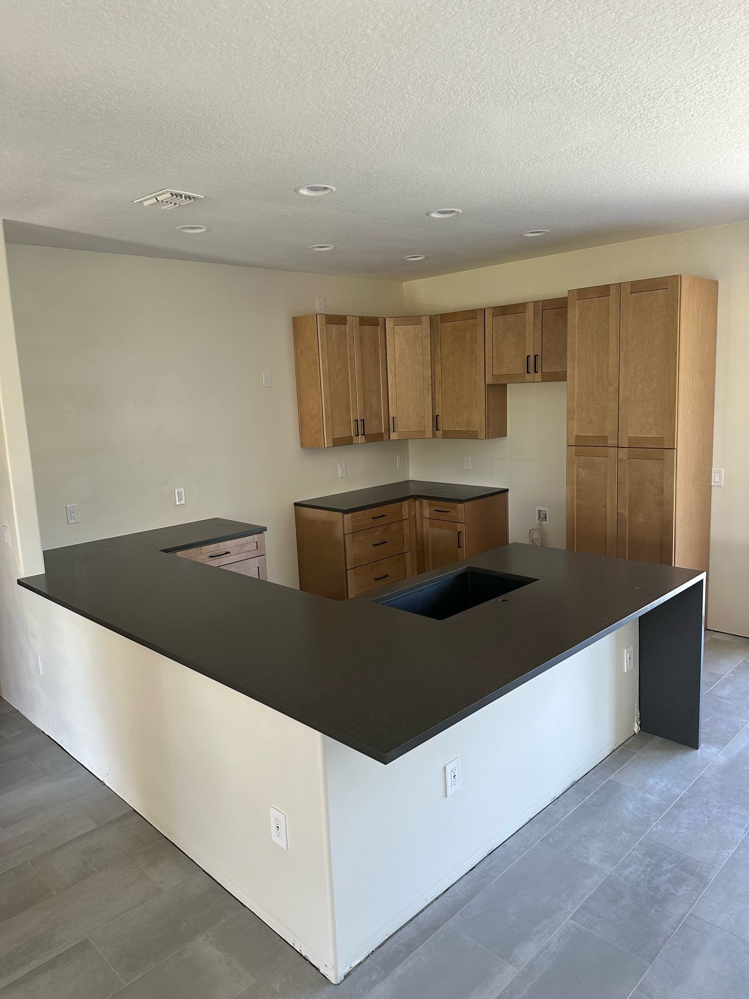 Natural maple shaker kitchen under construction with dark quartz peninsula countertop by 1 Stop Cabinets