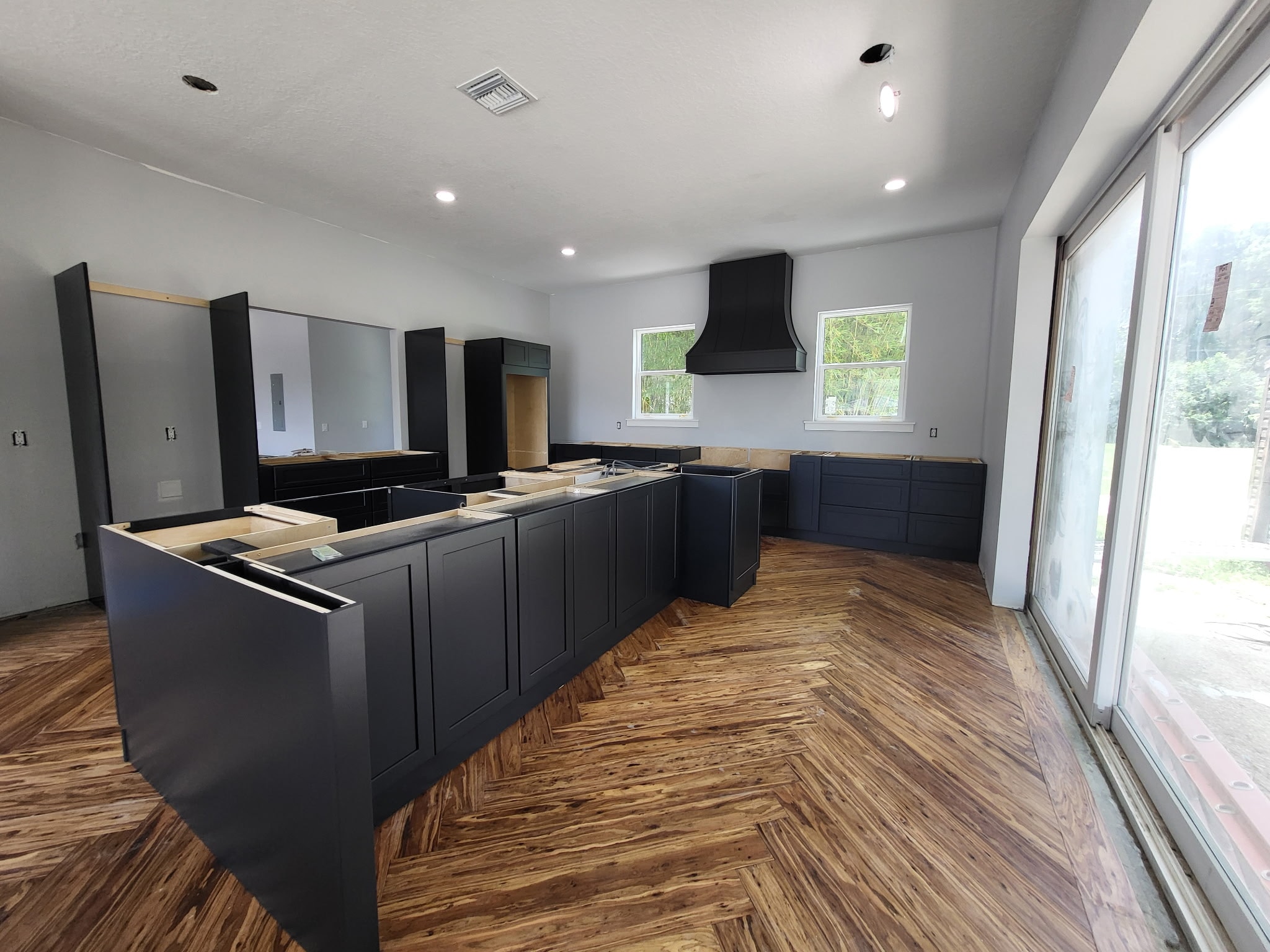 Dark navy shaker kitchen under construction with black range hood and herringbone wood floors by 1 Stop Cabinets
