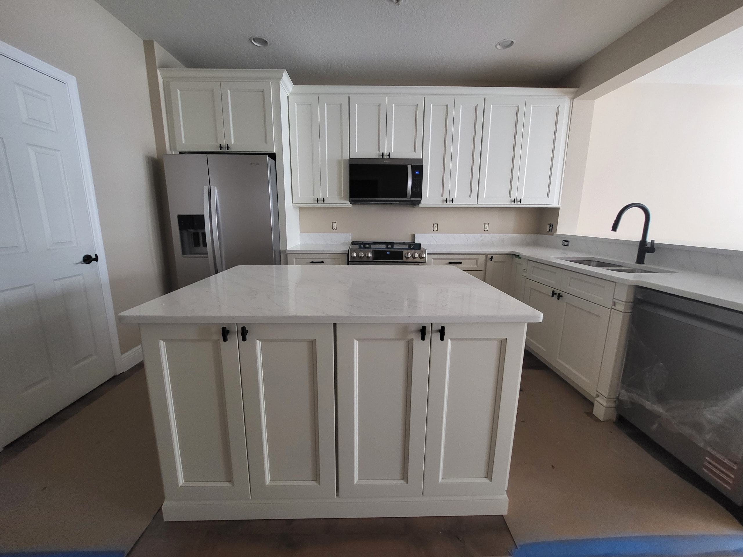White raised panel kitchen with quartz island and black hardware by 1 Stop Cabinets