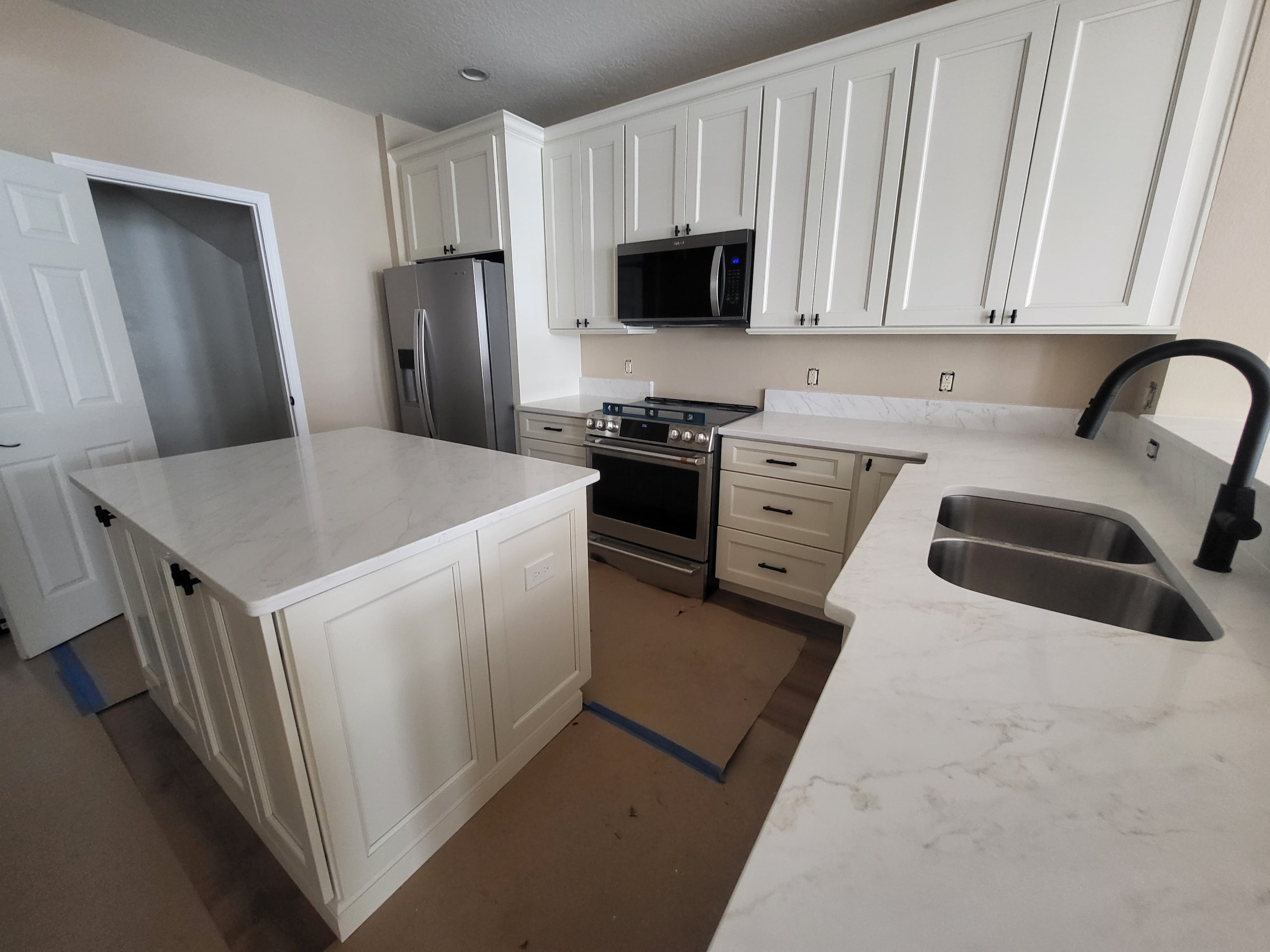White raised panel kitchen with quartz island and stainless double oven by 1 Stop Cabinets