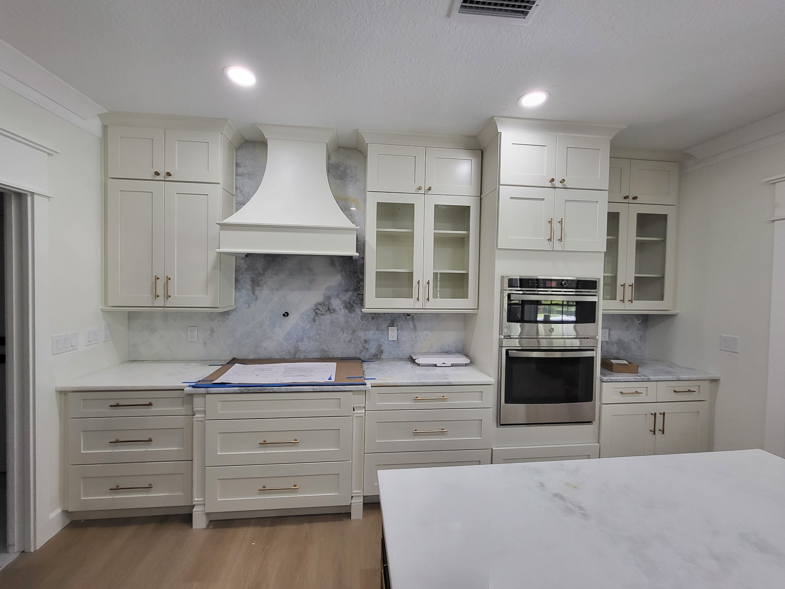 White shaker kitchen with dramatic marble backsplash and white range hood by 1 Stop Cabinets