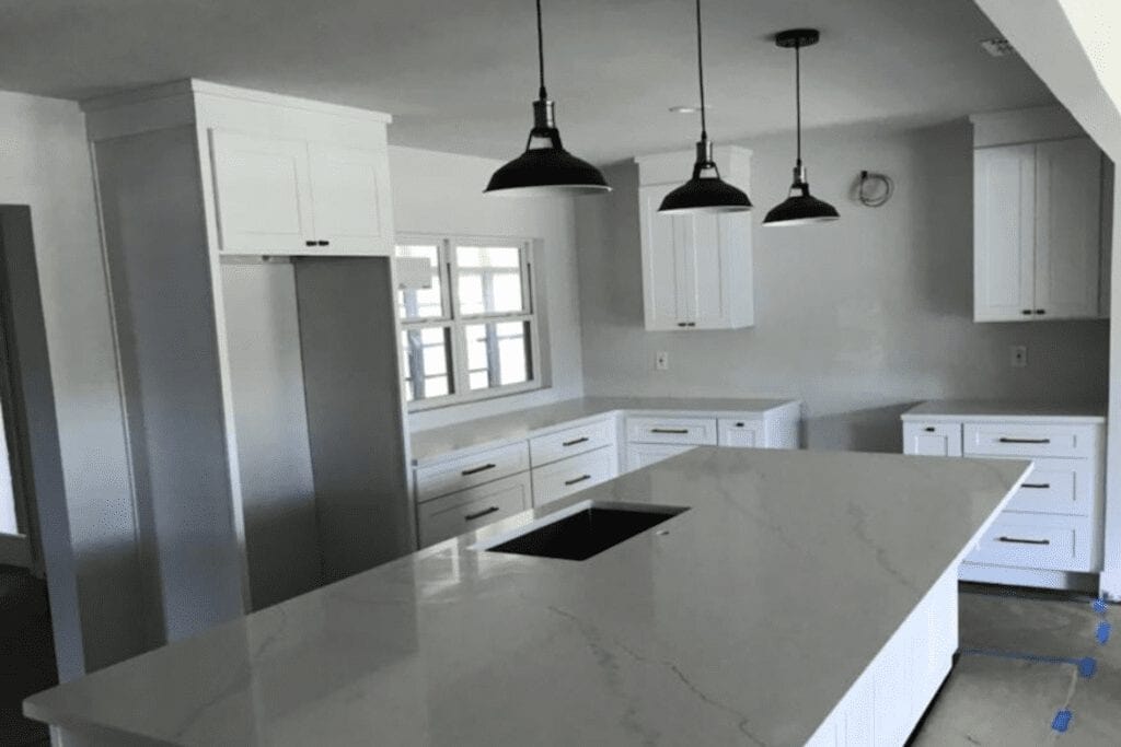 White shaker kitchen with quartz island and black pendants by 1 Stop Cabinets