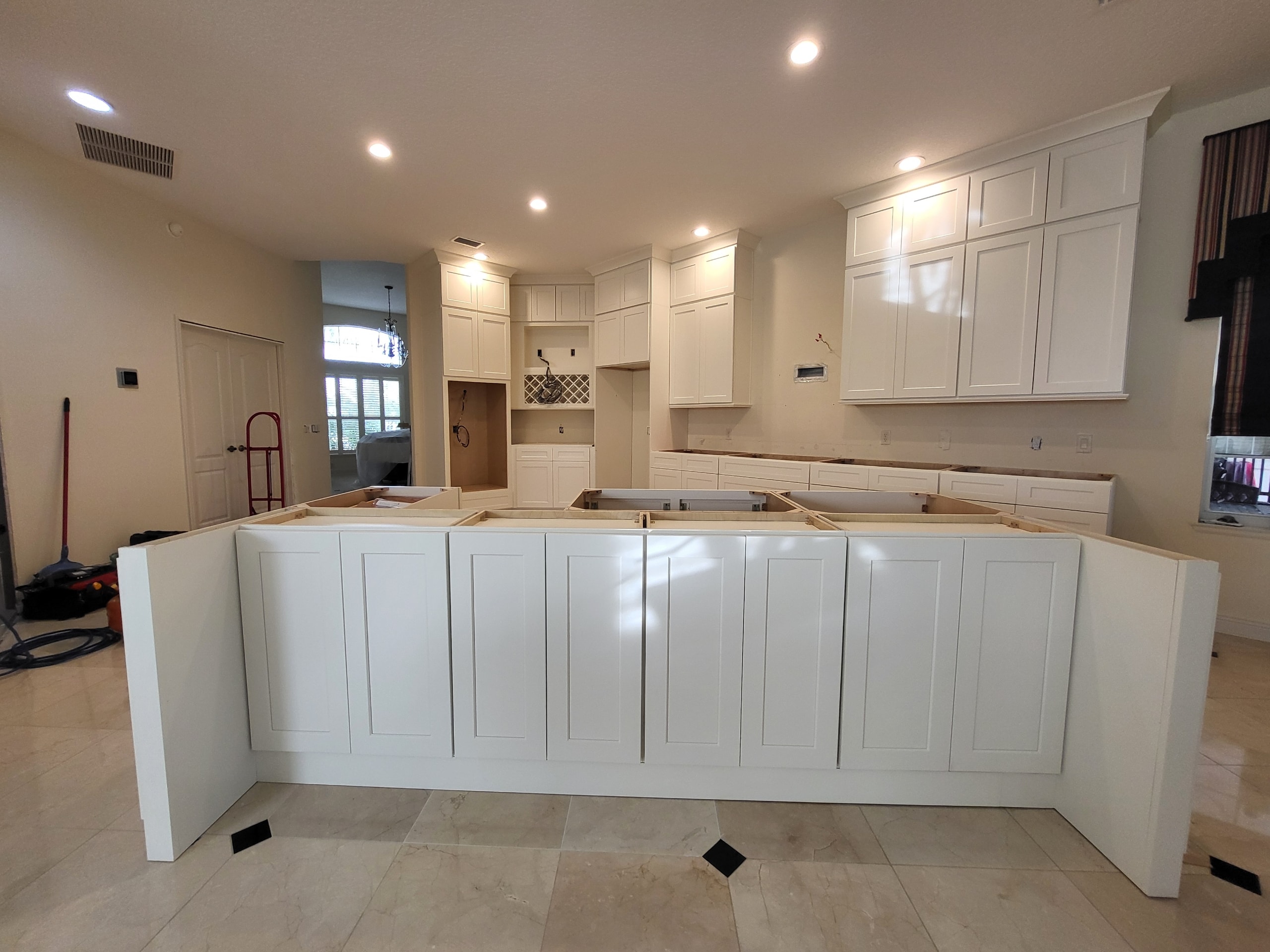 White shaker kitchen under construction showing island base cabinets on marble tile floors by 1 Stop Cabinets