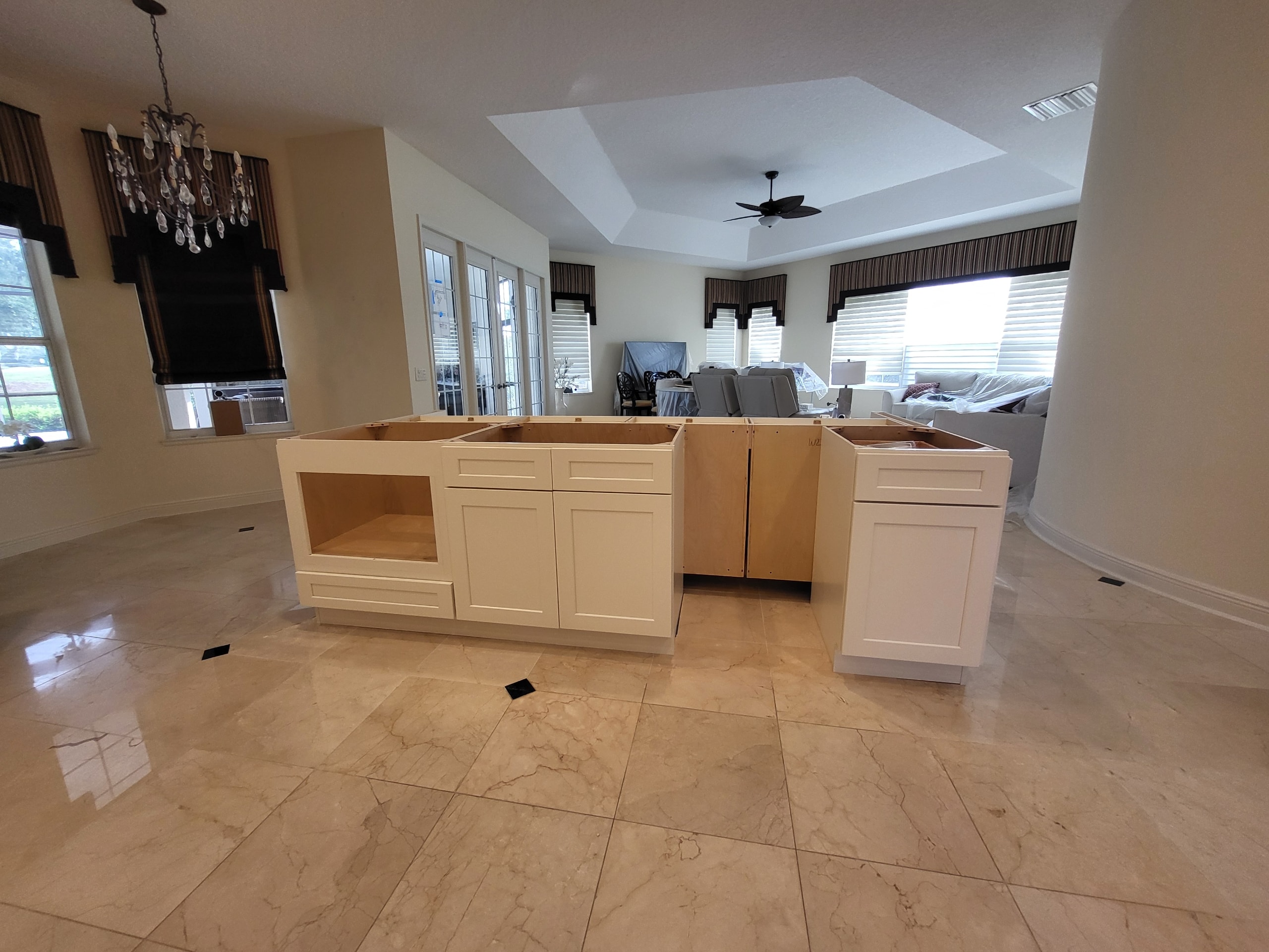 White shaker kitchen under construction with large island and open concept layout on marble floors by 1 Stop Cabinets