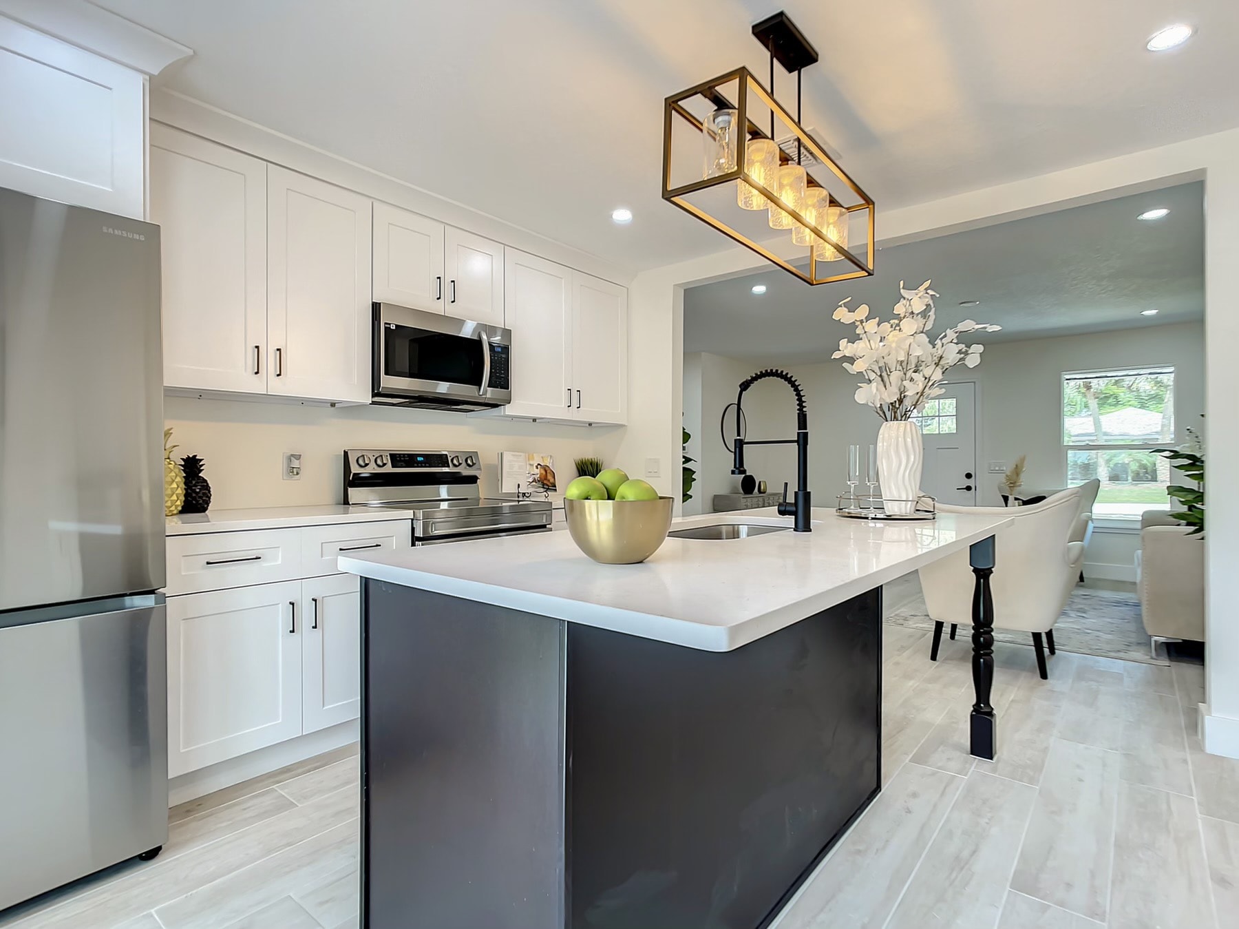 White and black two-tone kitchen with quartz island and brass cage pendant from dining angle by 1 Stop Cabinets