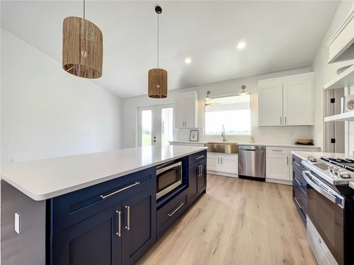 White and navy blue kitchen with quartz island built-in microwave and rattan pendants by 1 Stop Cabinets